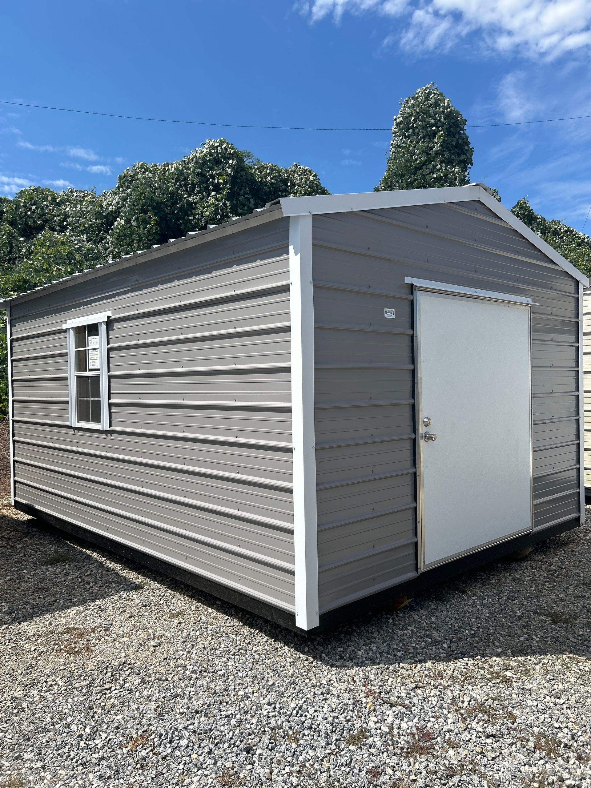 Small gray portable building with white roll-up door and window, sitting on gravel under a blue sky