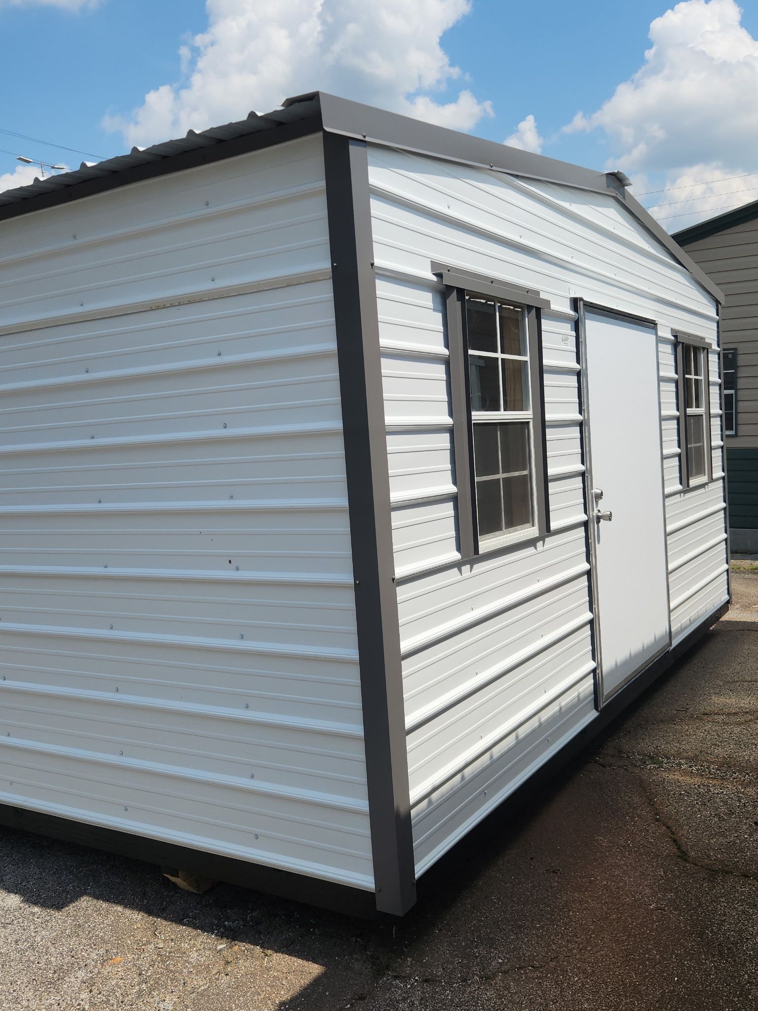 White portable shed with black trim and windows on a gravel lot under a blue sky