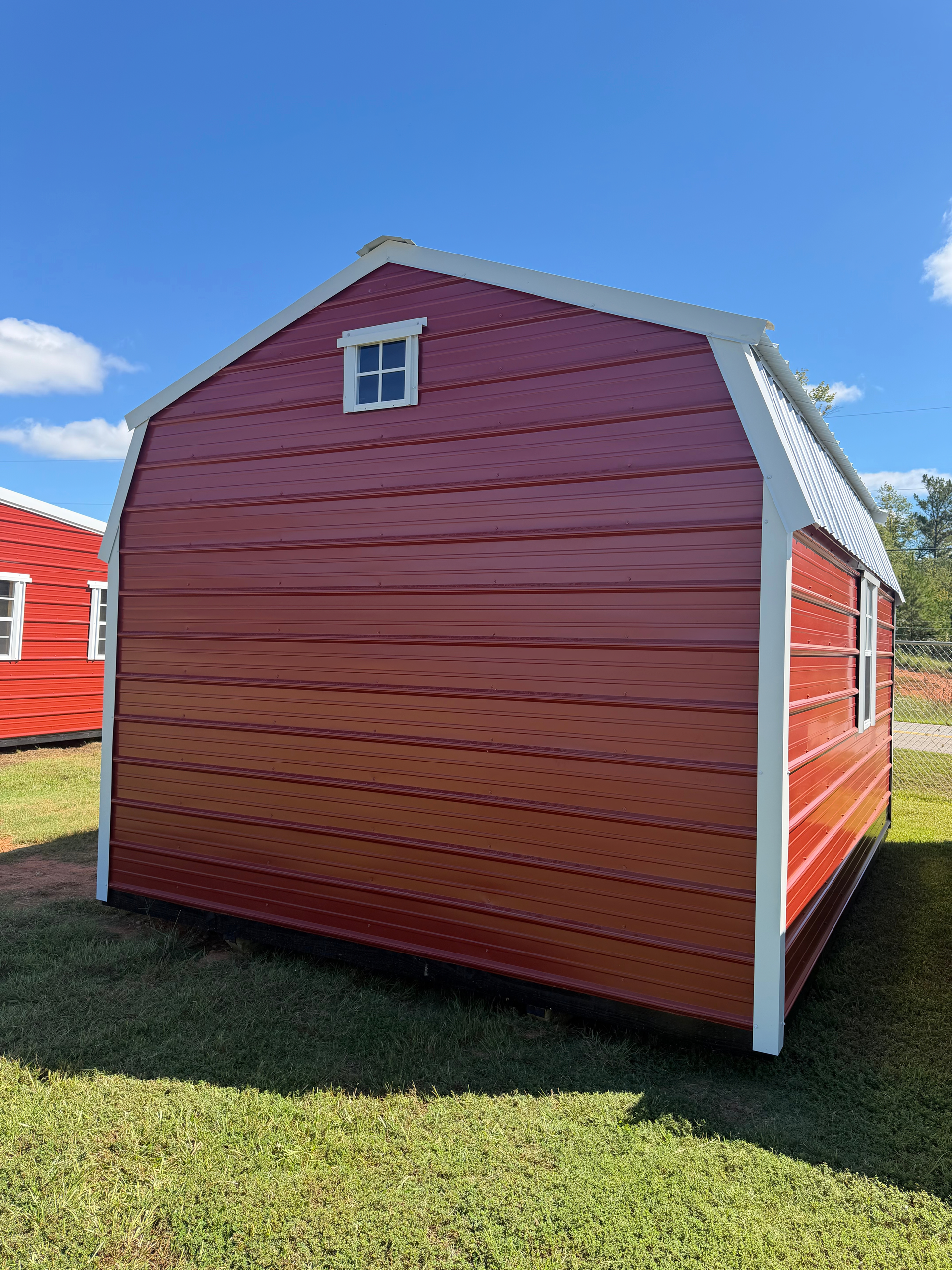 Red shed with white trim and small window on a grassy lot under a blue sky
