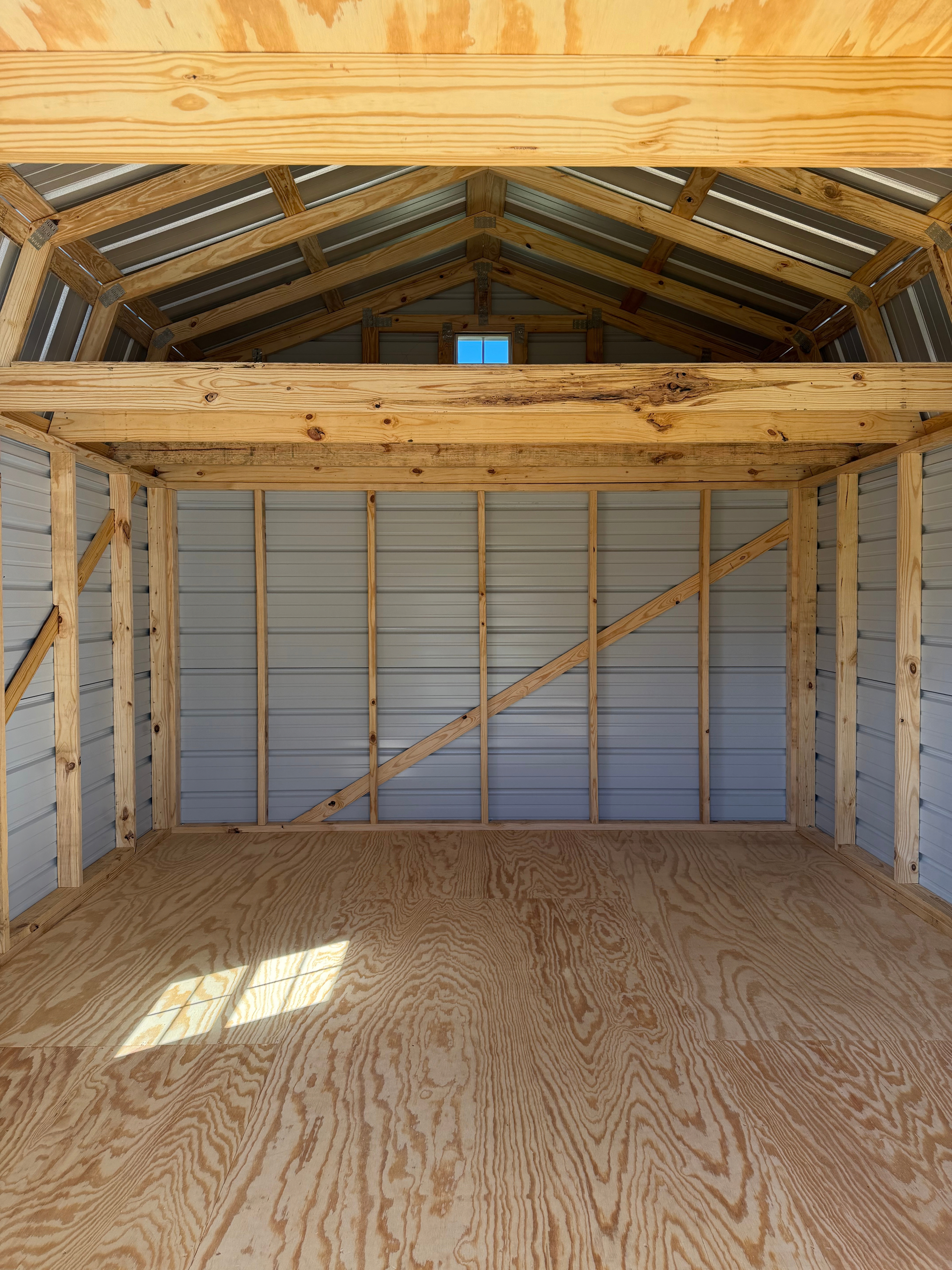 Interior of a wooden shed under construction, with exposed framing and plywood floor under a vaulted roof.