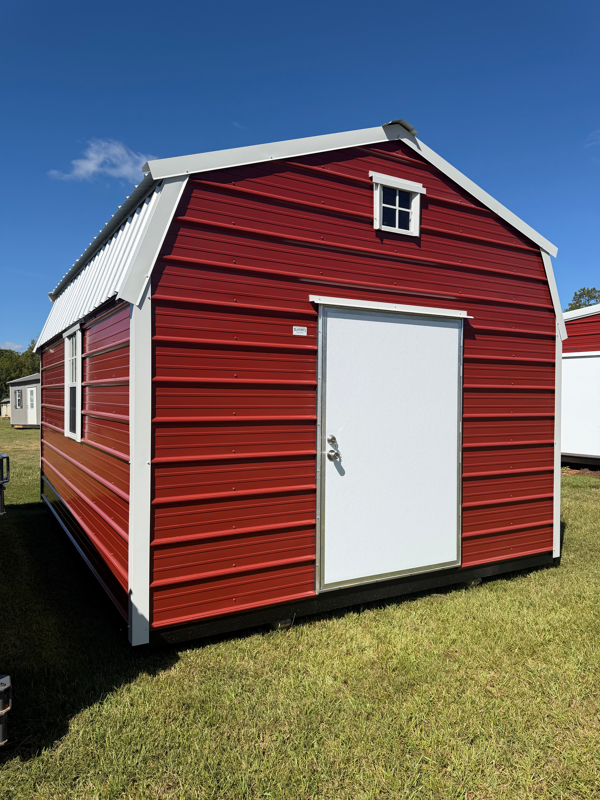 Red barn-style storage shed with white trim and door, sitting on grass under a blue sky