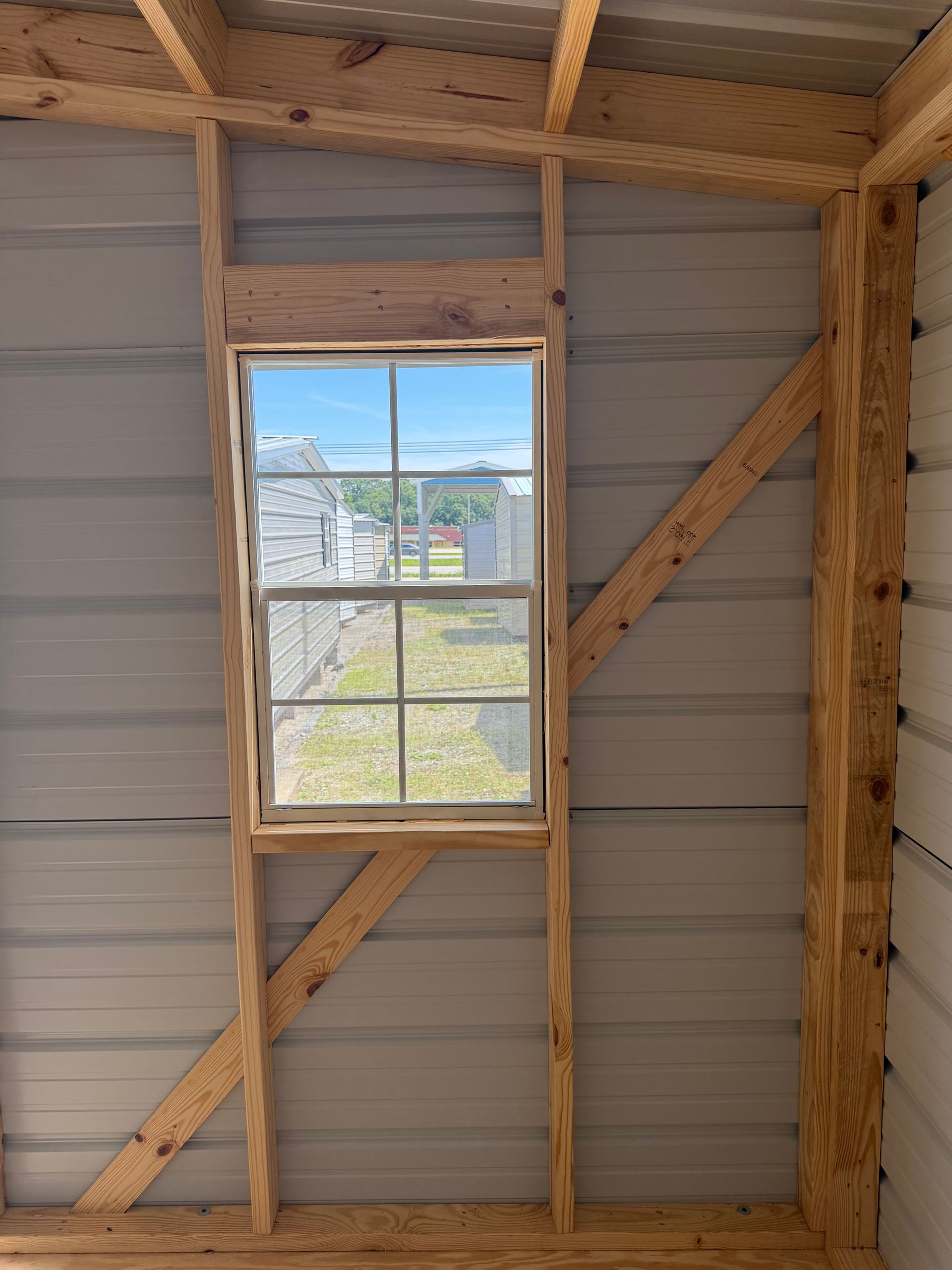 Interior wall with a window framing a view of rooftops, trees, and blue sky during construction