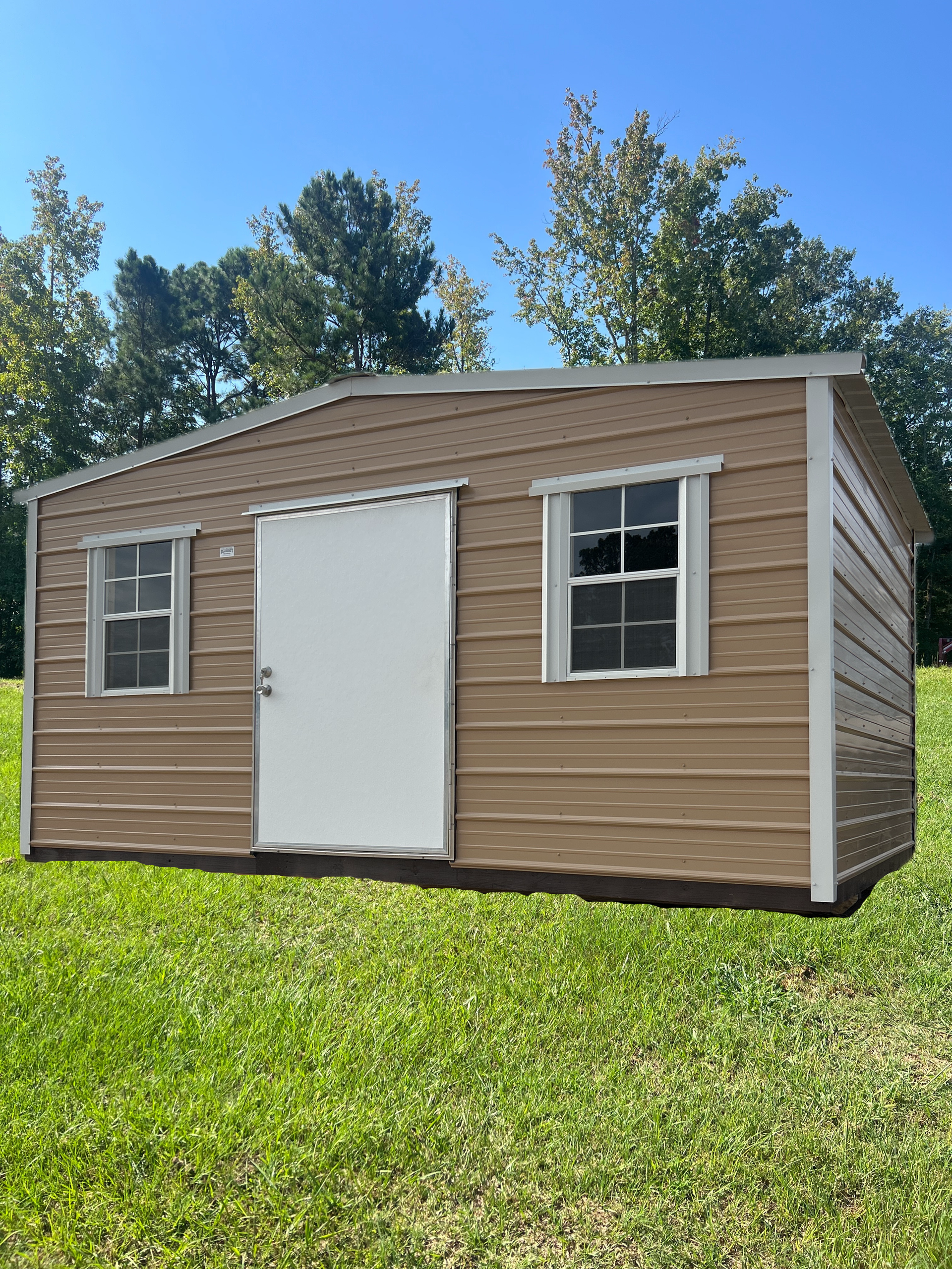 Small tan shed with white door and windows on a grassy lawn under a blue sky