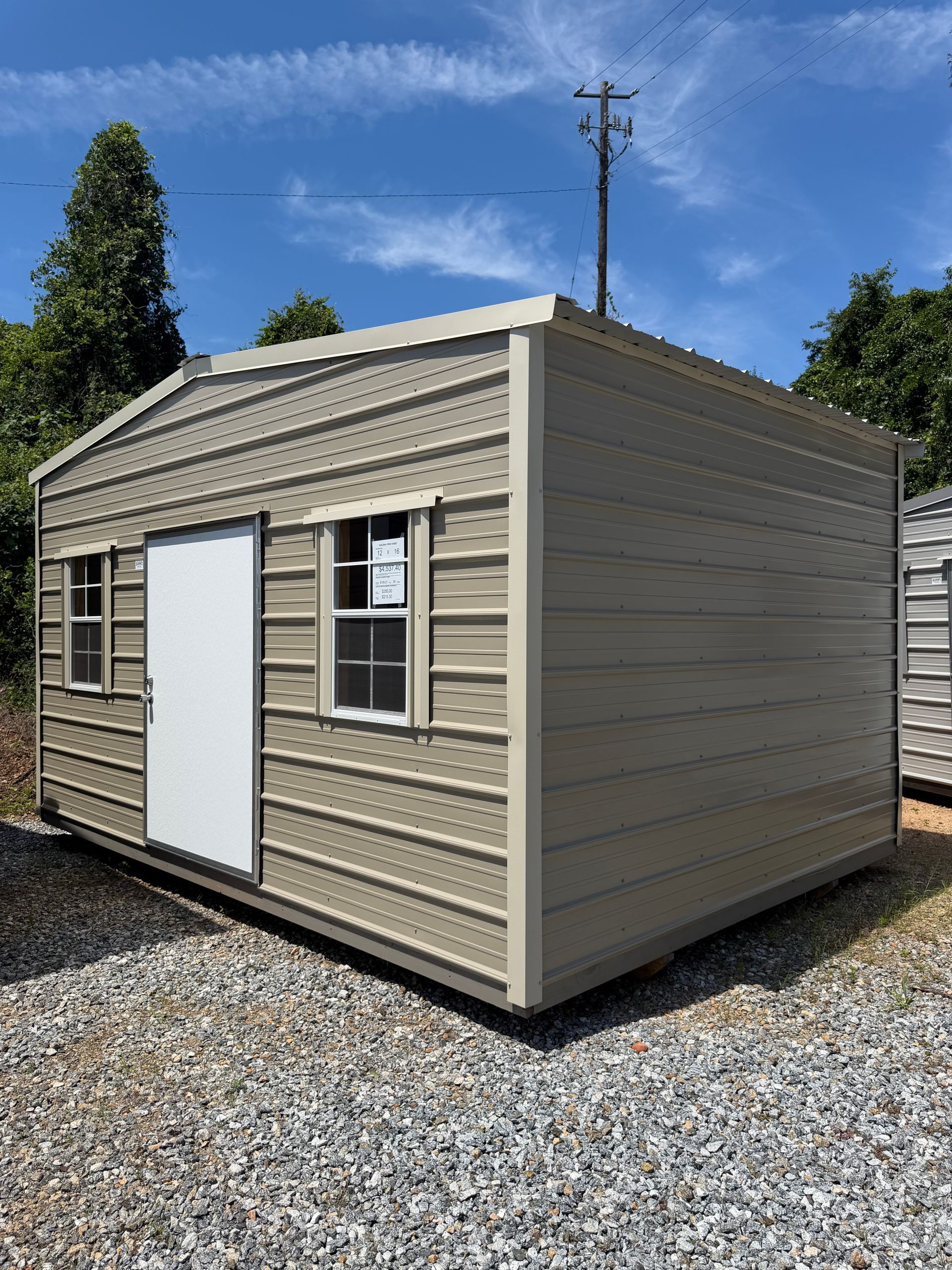 Small beige shed with white doors and windows in a yard under trees.