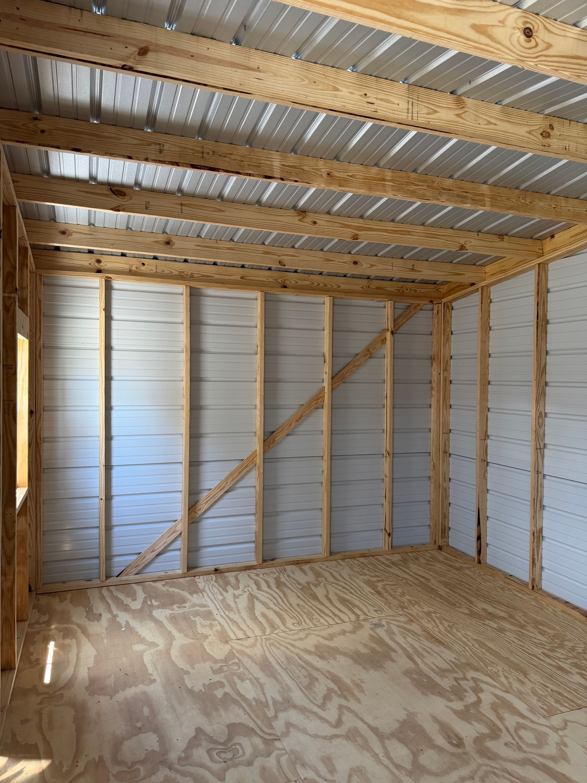 Interior of an unfinished wooden shed with plywood floor and exposed studs and rafters