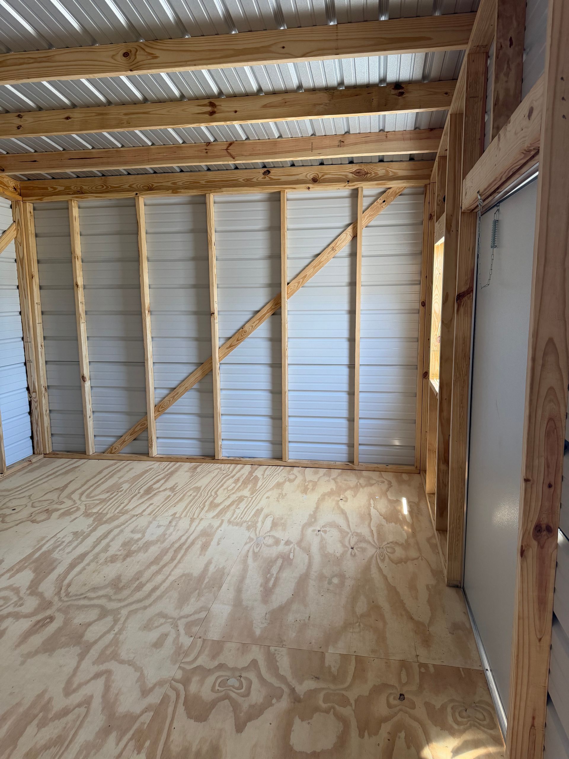 Empty unfinished room with plywood floor, exposed studs, and insulated walls under a slanted roof.