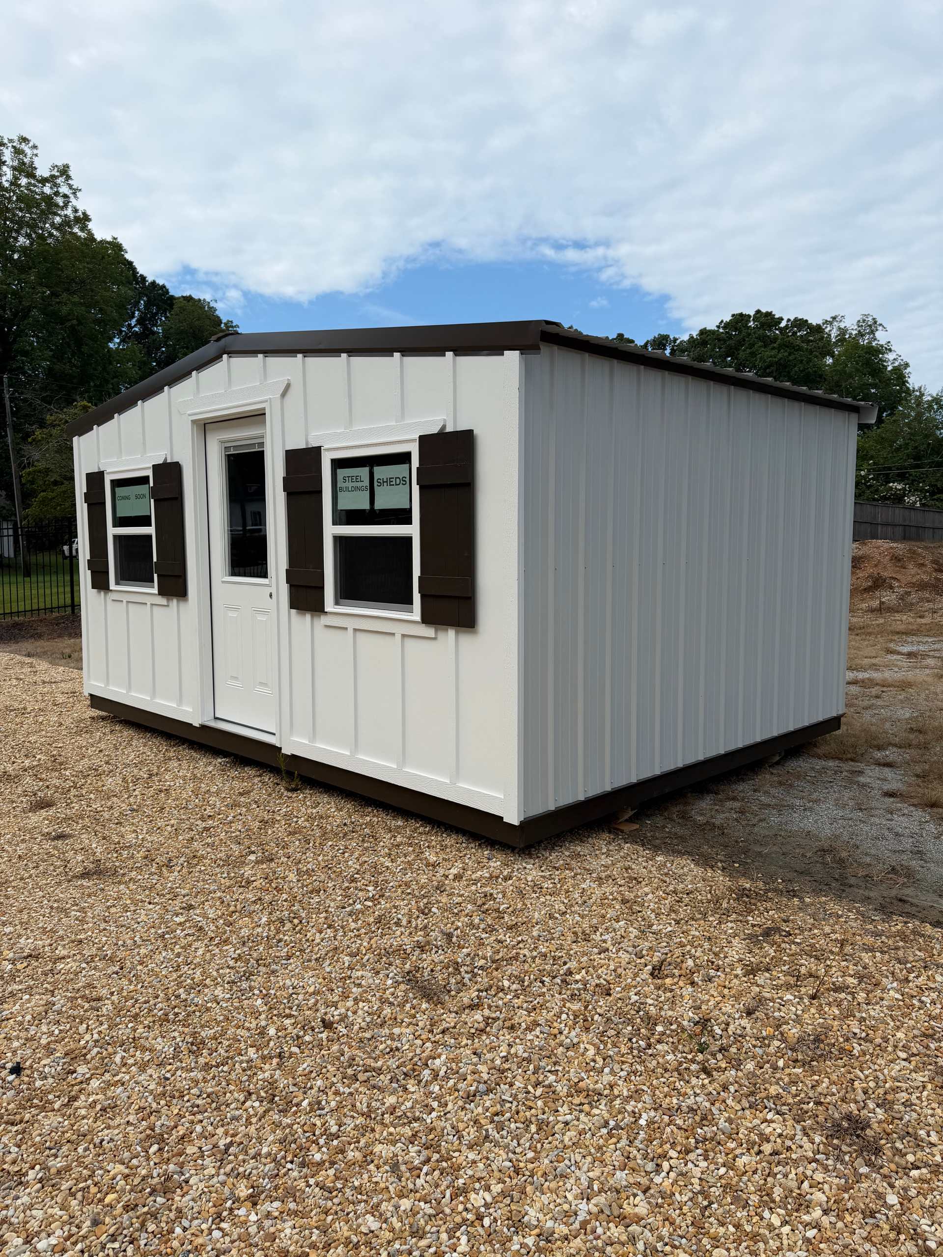 Small white portable building with dark shutters on a gravel lot under a blue sky