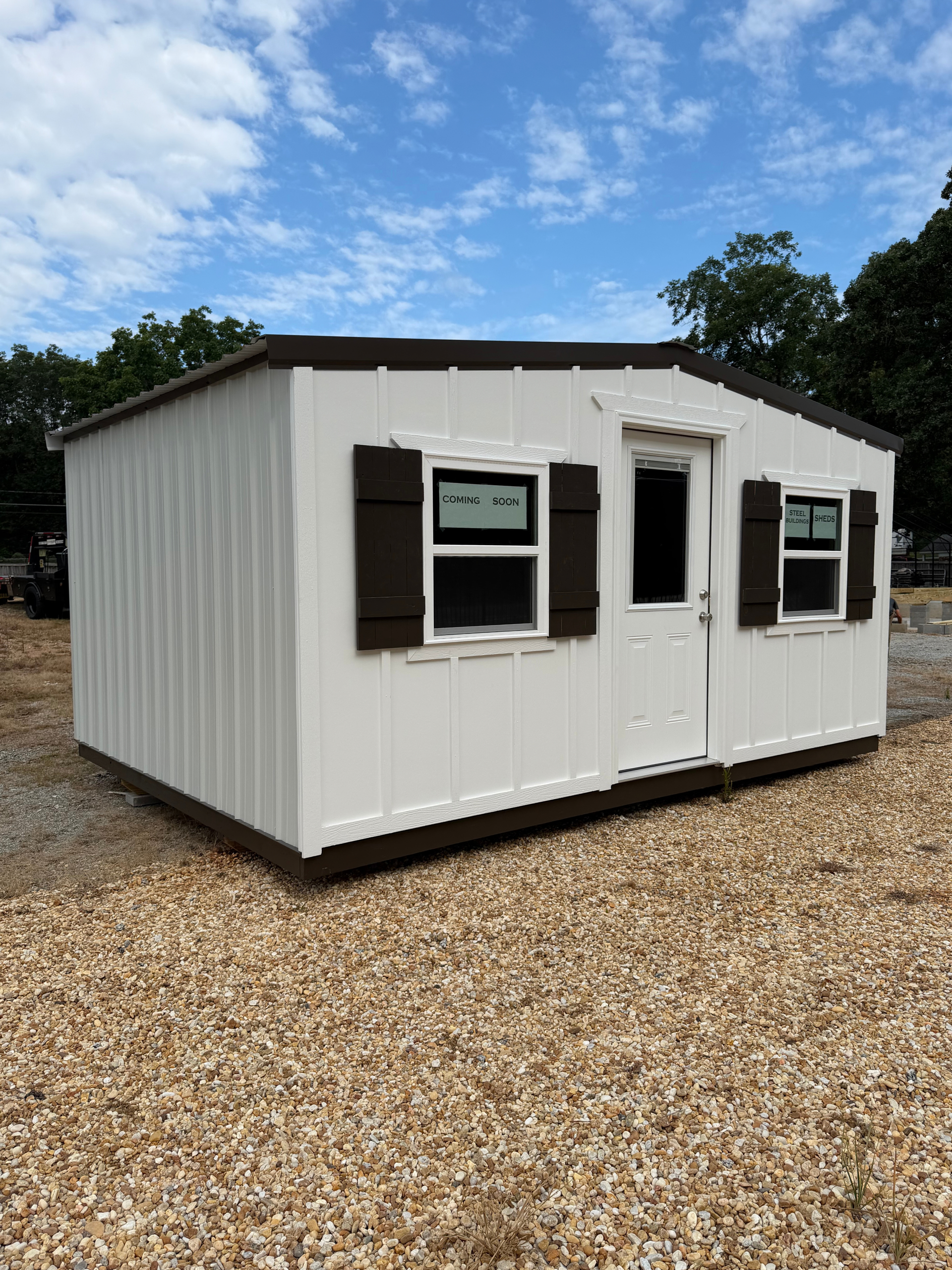 Small white portable building with brown trim and windows, sitting on gravel under a blue sky.
