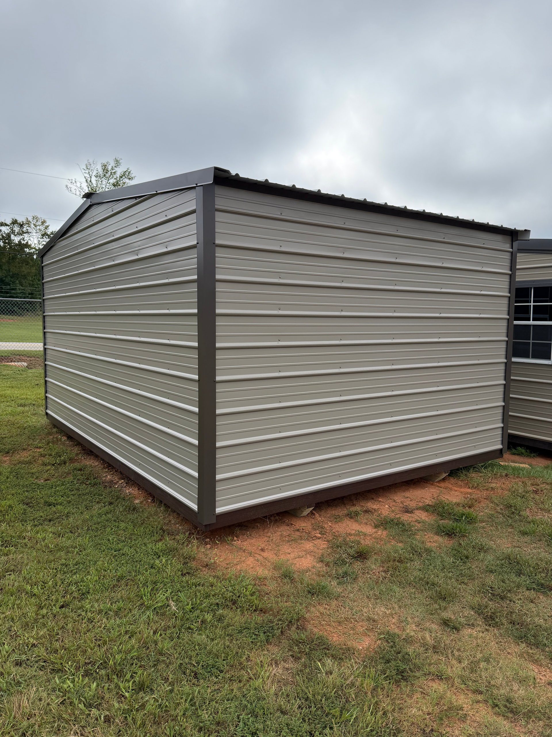 Beige metal shed with dark trim on a grassy lot under a cloudy sky