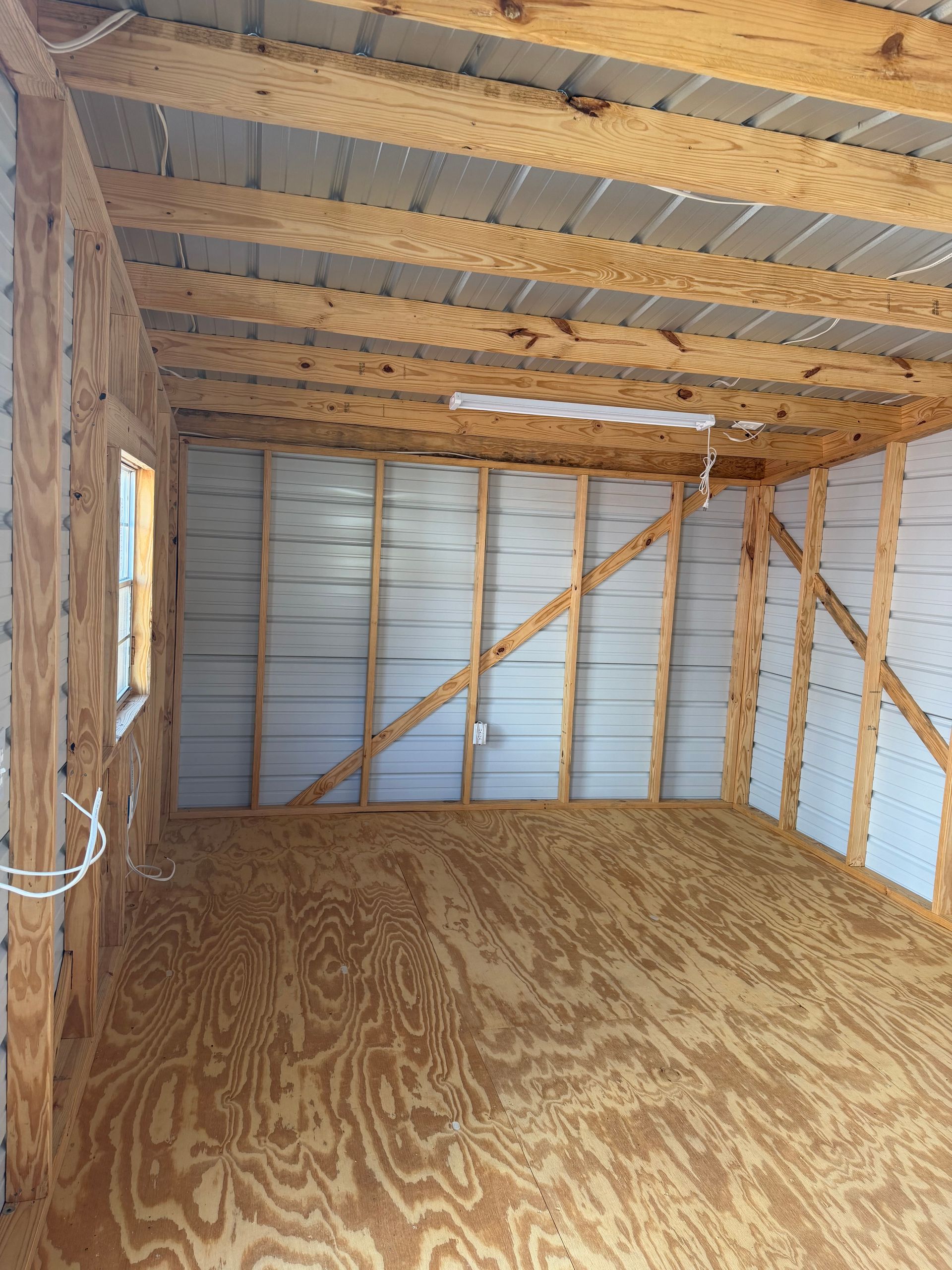 Empty wooden storage shed interior with plywood floor and exposed framing