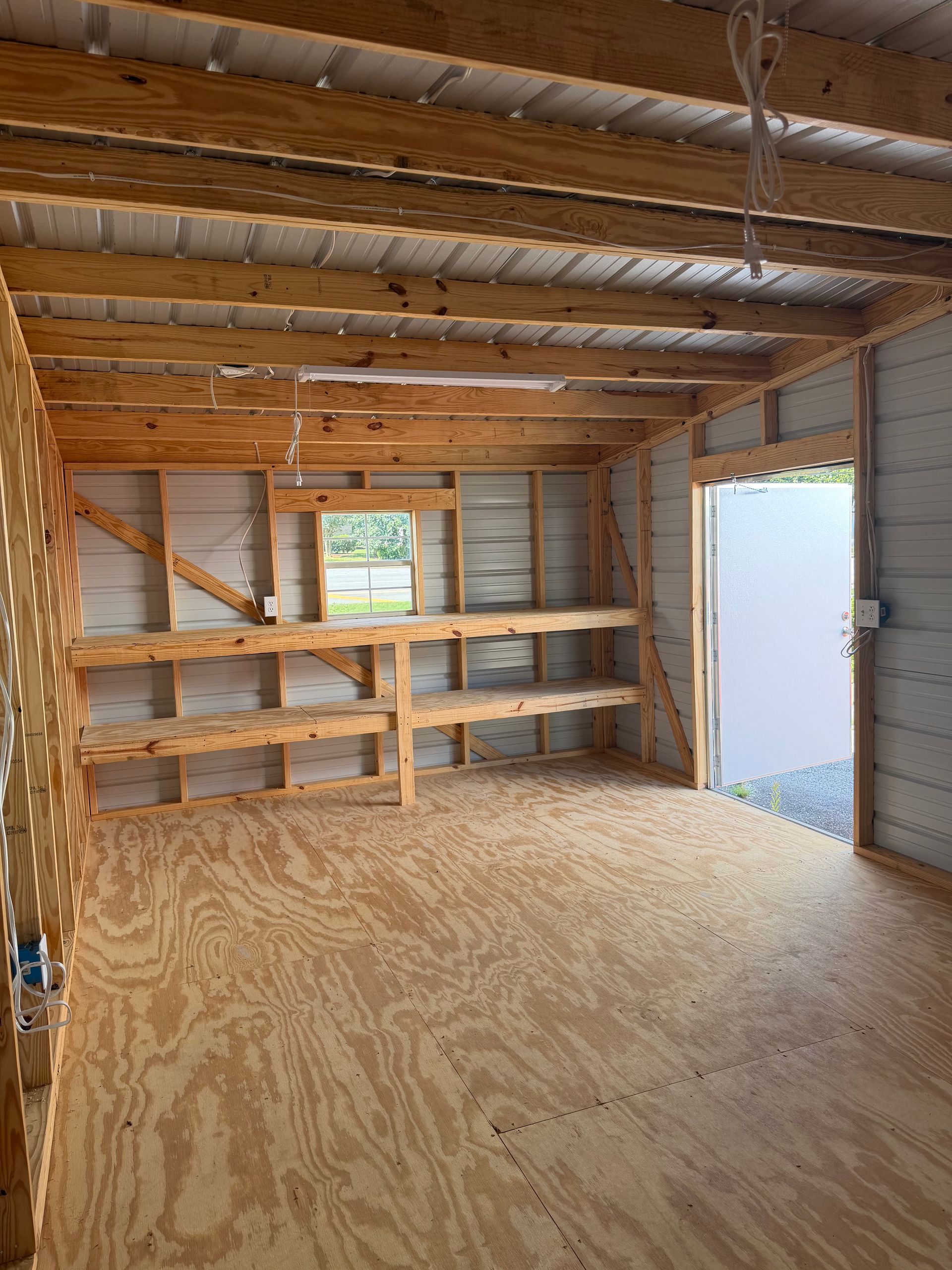 Unfinished garage interior with exposed beams, plywood shelves, and a white door on the right.