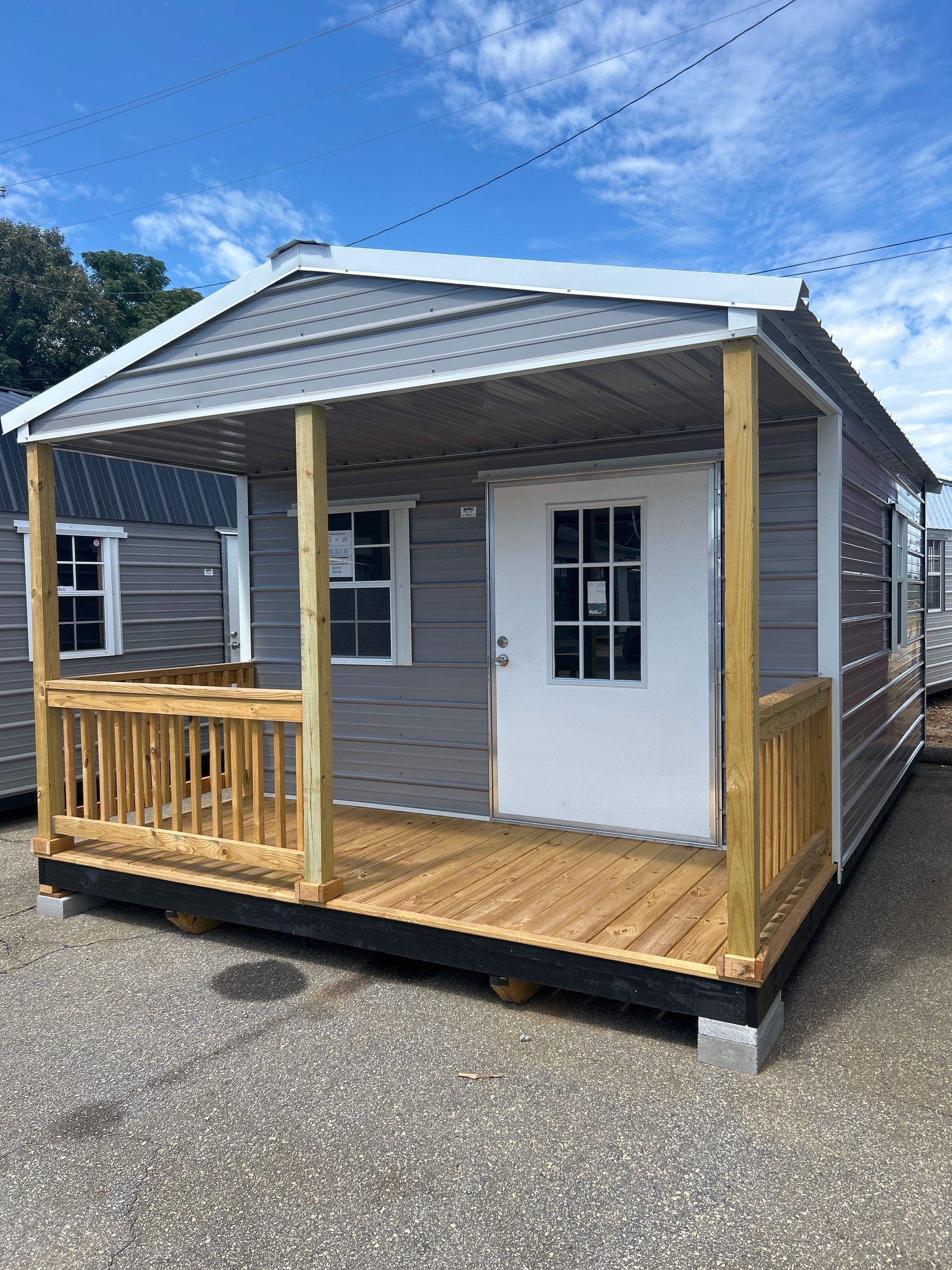 Small gray porch cabin with white door, wood railing, and wooden deck under a blue sky