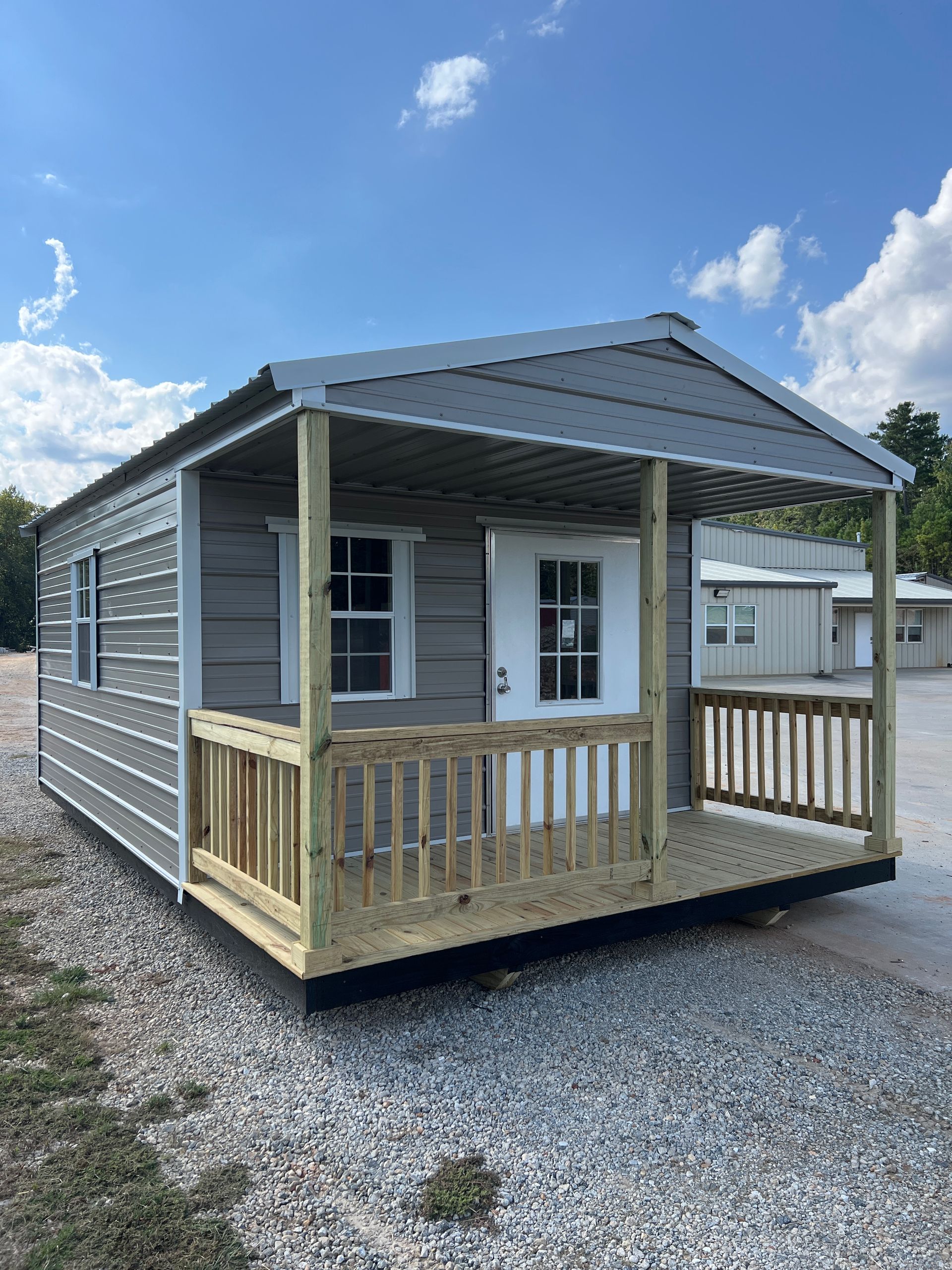 Gray mobile home with a small covered porch and railings on a gravel lot under a blue sky