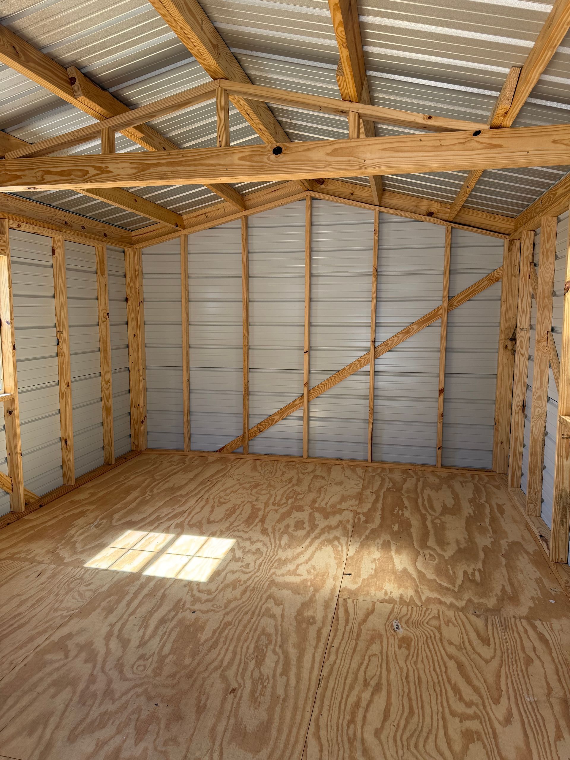 Empty unfinished wooden shed interior with plywood floor and exposed beams