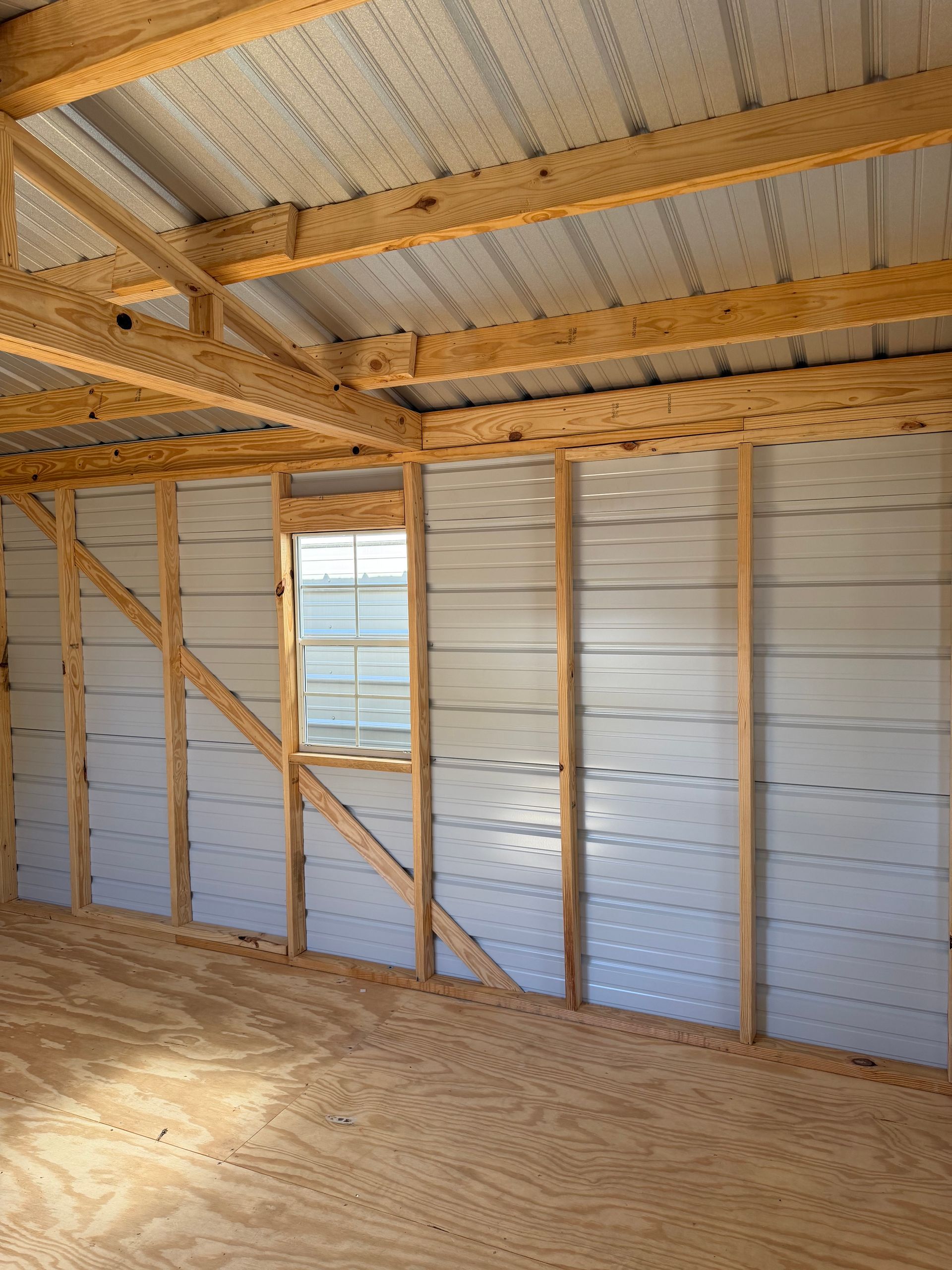 Interior of an unfinished wooden shed with plywood floor, exposed framing, and a small window showing outside.