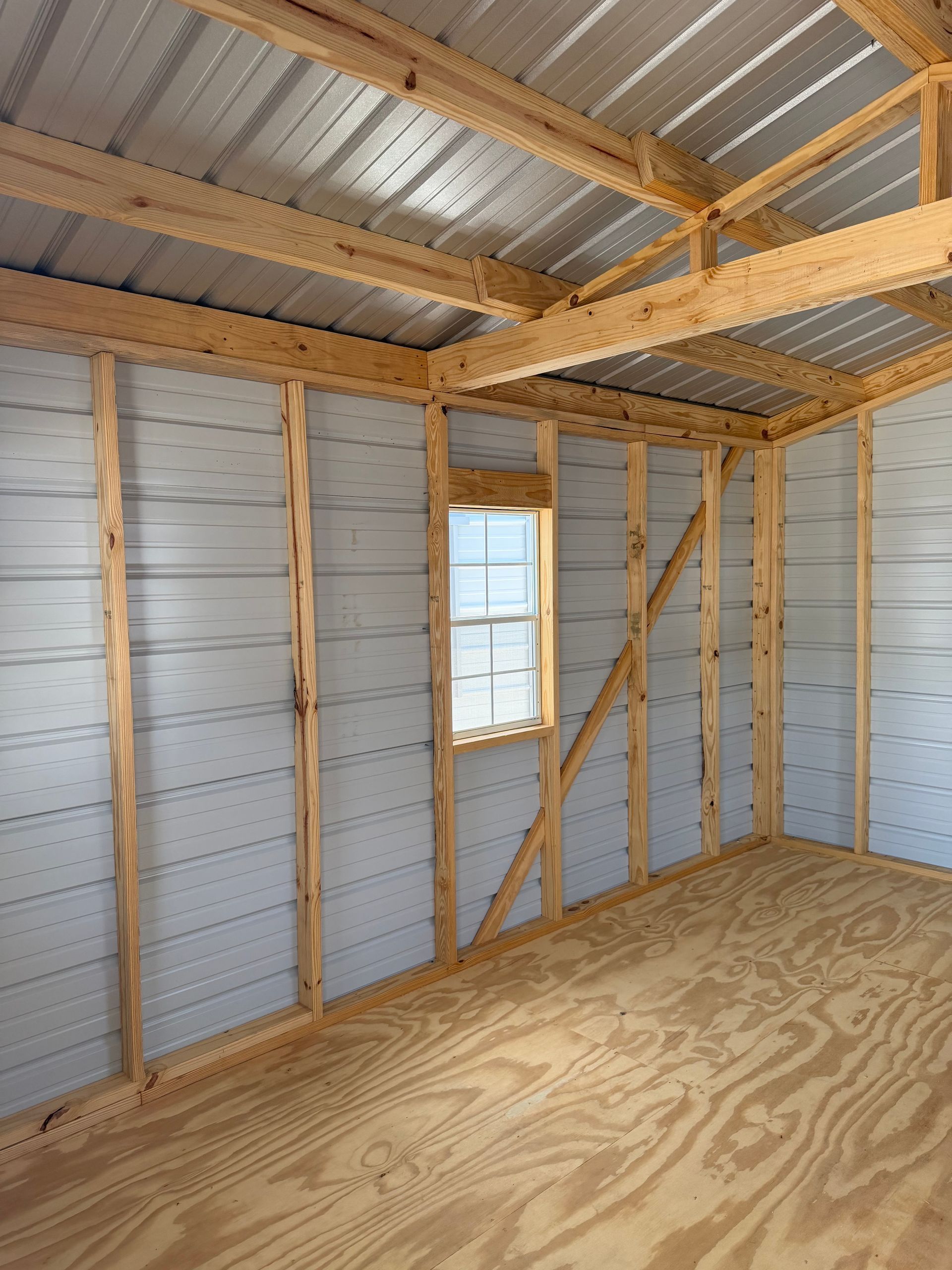 Inside a small unfinished room with plywood floor, exposed wood framing, and a single window.