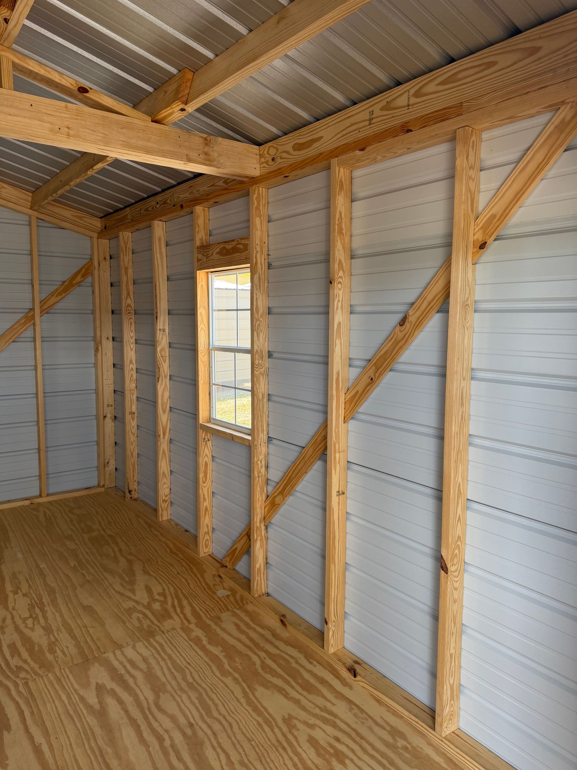 Interior of an unfinished shed with exposed wooden framing, corrugated metal walls, and plywood floor.