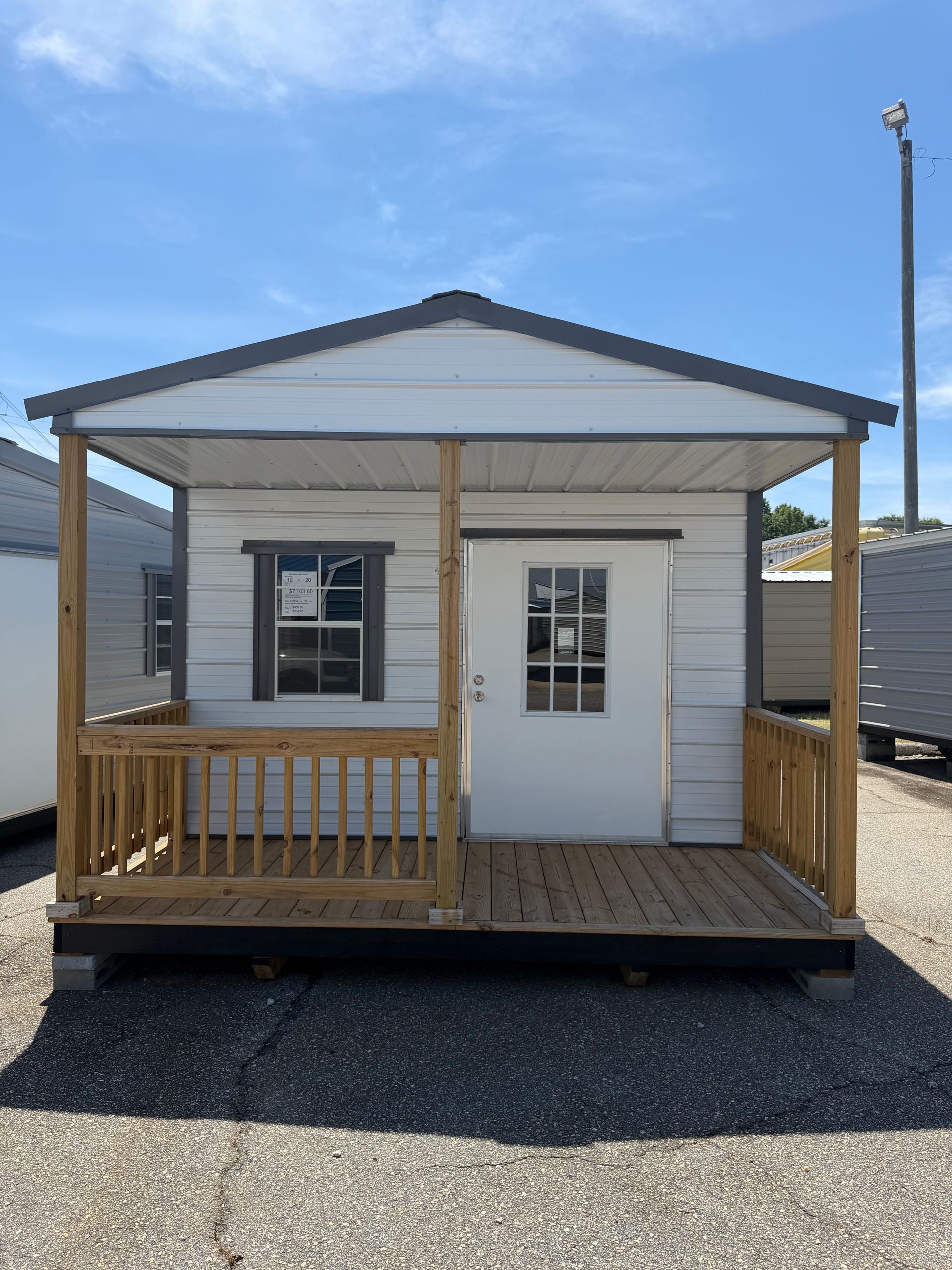 Small white modular cabin with porch and ramp on a gravel lot under a blue sky.