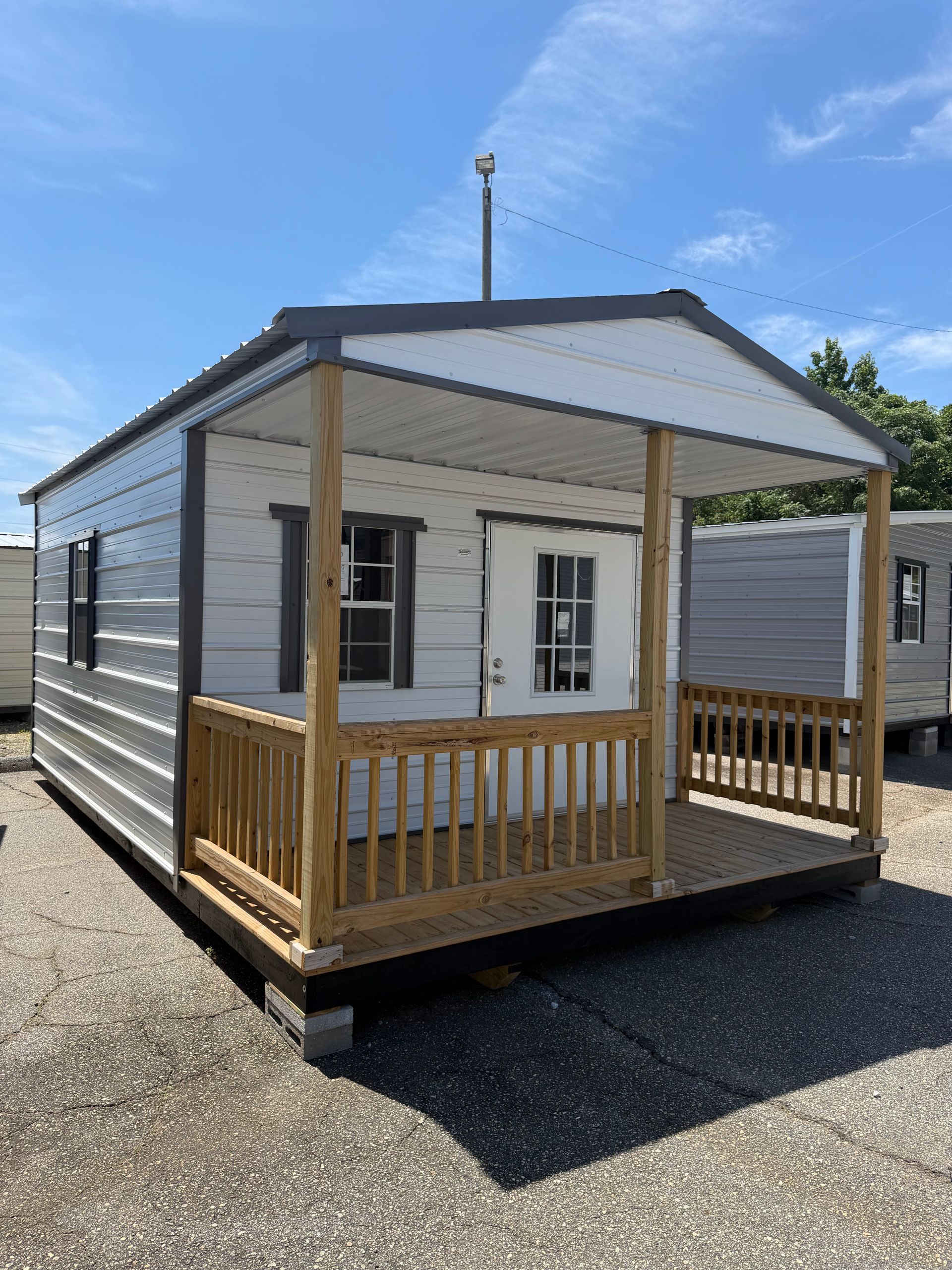 Small white portable office cabin with a front porch and blue side panel on a paved lot