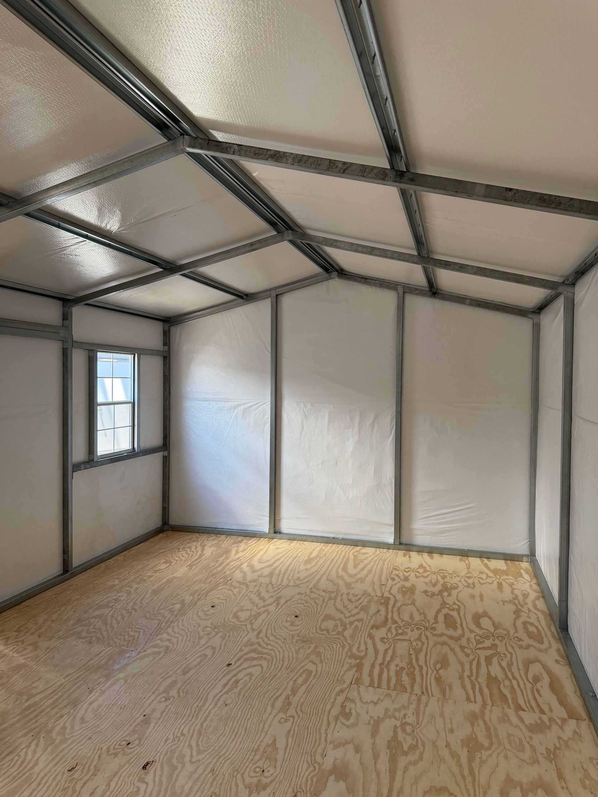 Empty unfinished shed interior with plywood floor, insulated walls, and exposed metal roof framing.