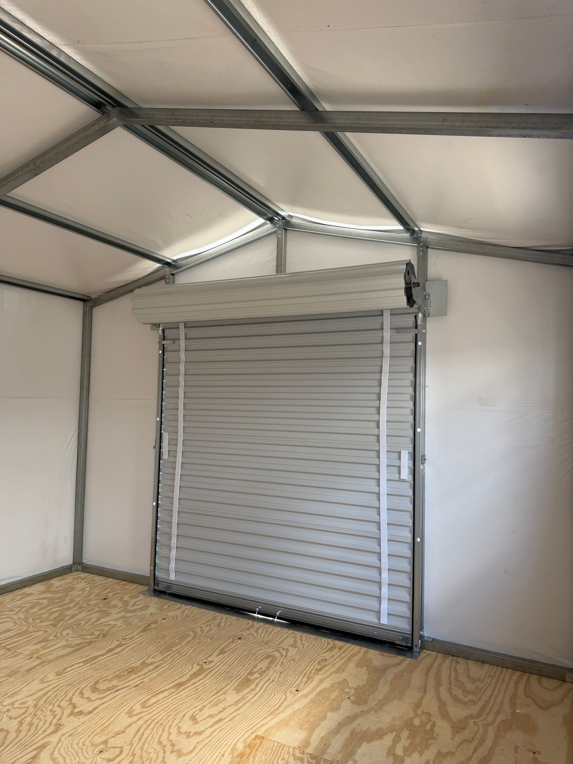 Small room with a gray roll-up door, white walls, metal ceiling beams, and patterned carpet.