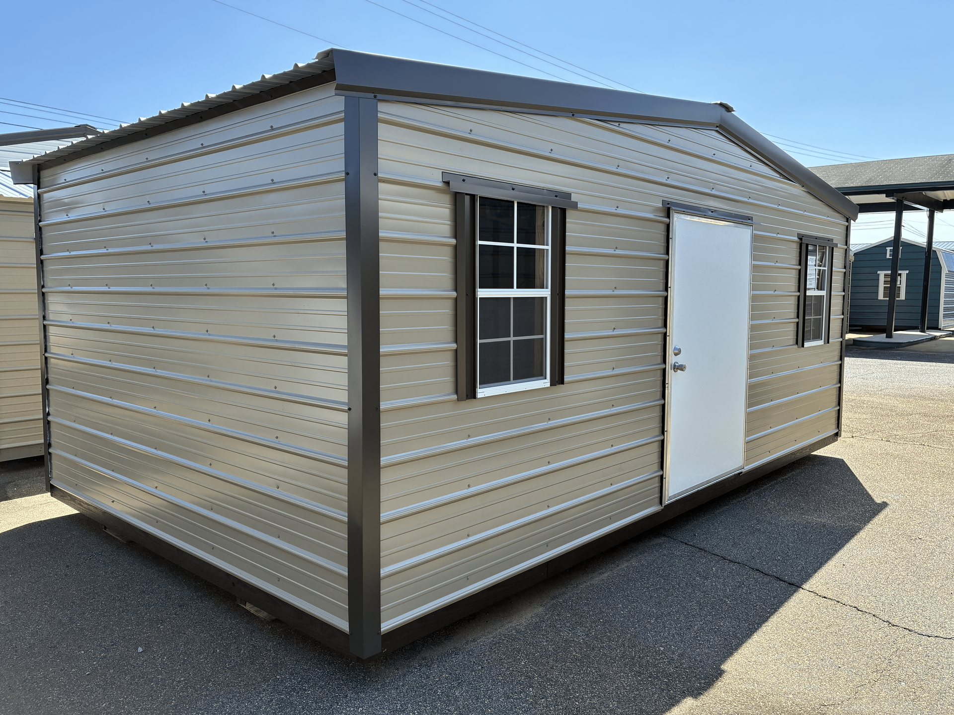 Small beige portable shed with gray trim, a window, and a white door on a gravel lot