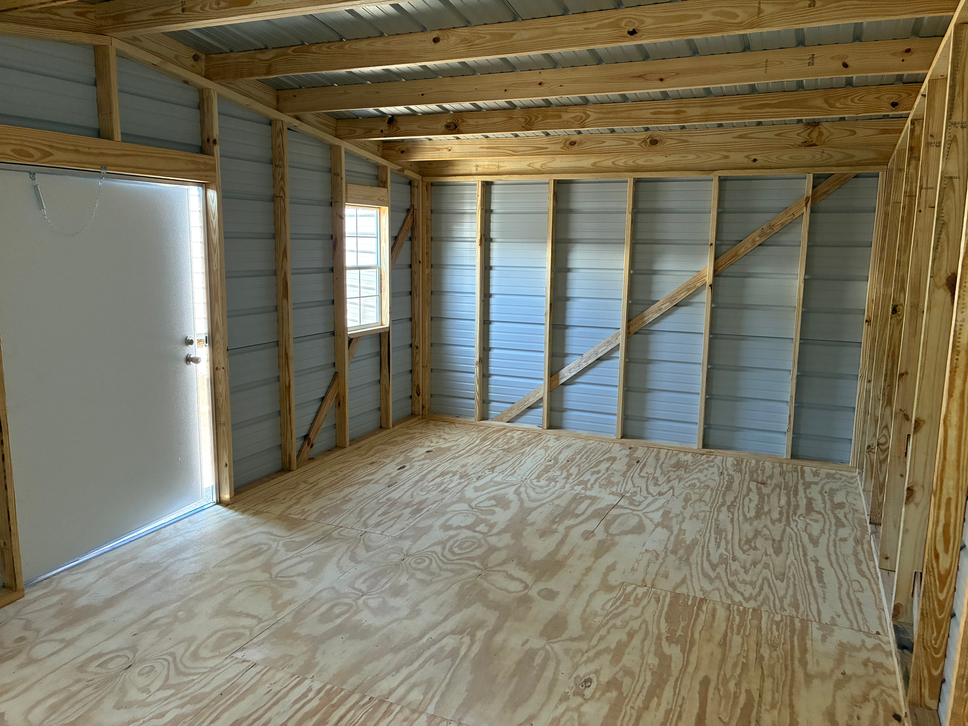 Empty unfinished room with plywood floor, exposed wood framing, and insulated walls and ceiling