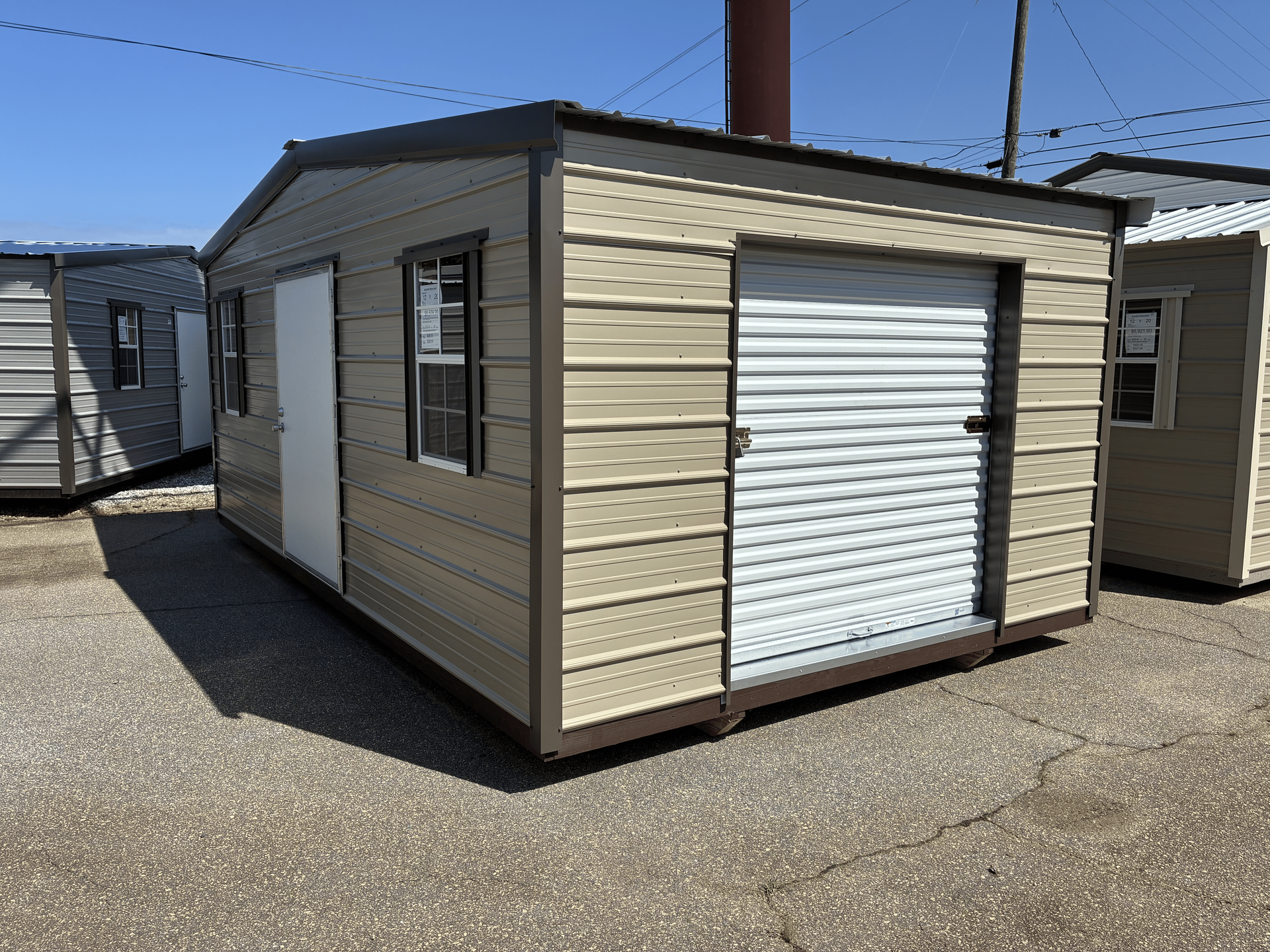 Portable beige storage shed with white roll-up door in an outdoor lot
