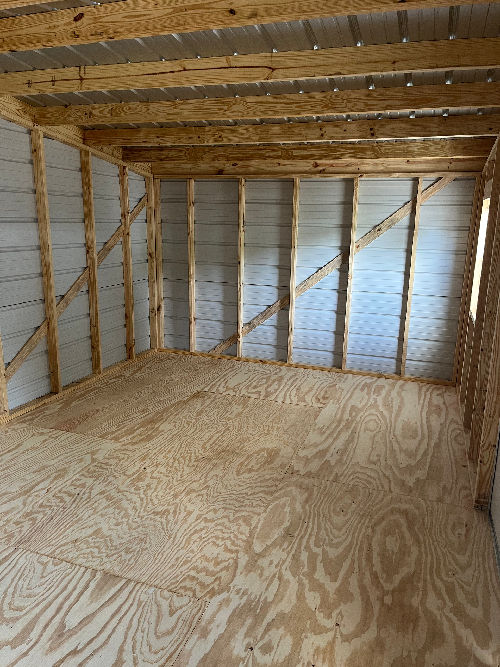 Empty unfinished room with exposed wooden framing, plywood floor, and insulated walls under construction