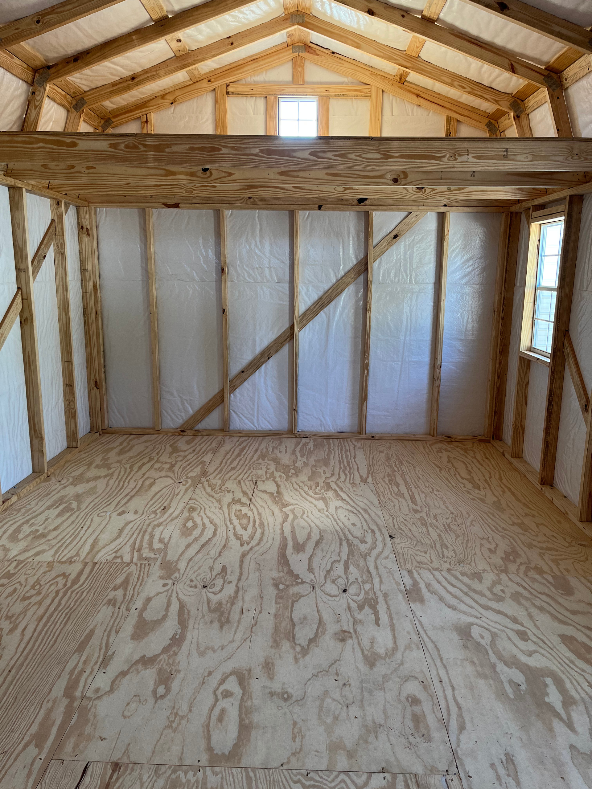 Empty wooden loft interior with plywood floor, exposed framing, and two small windows.