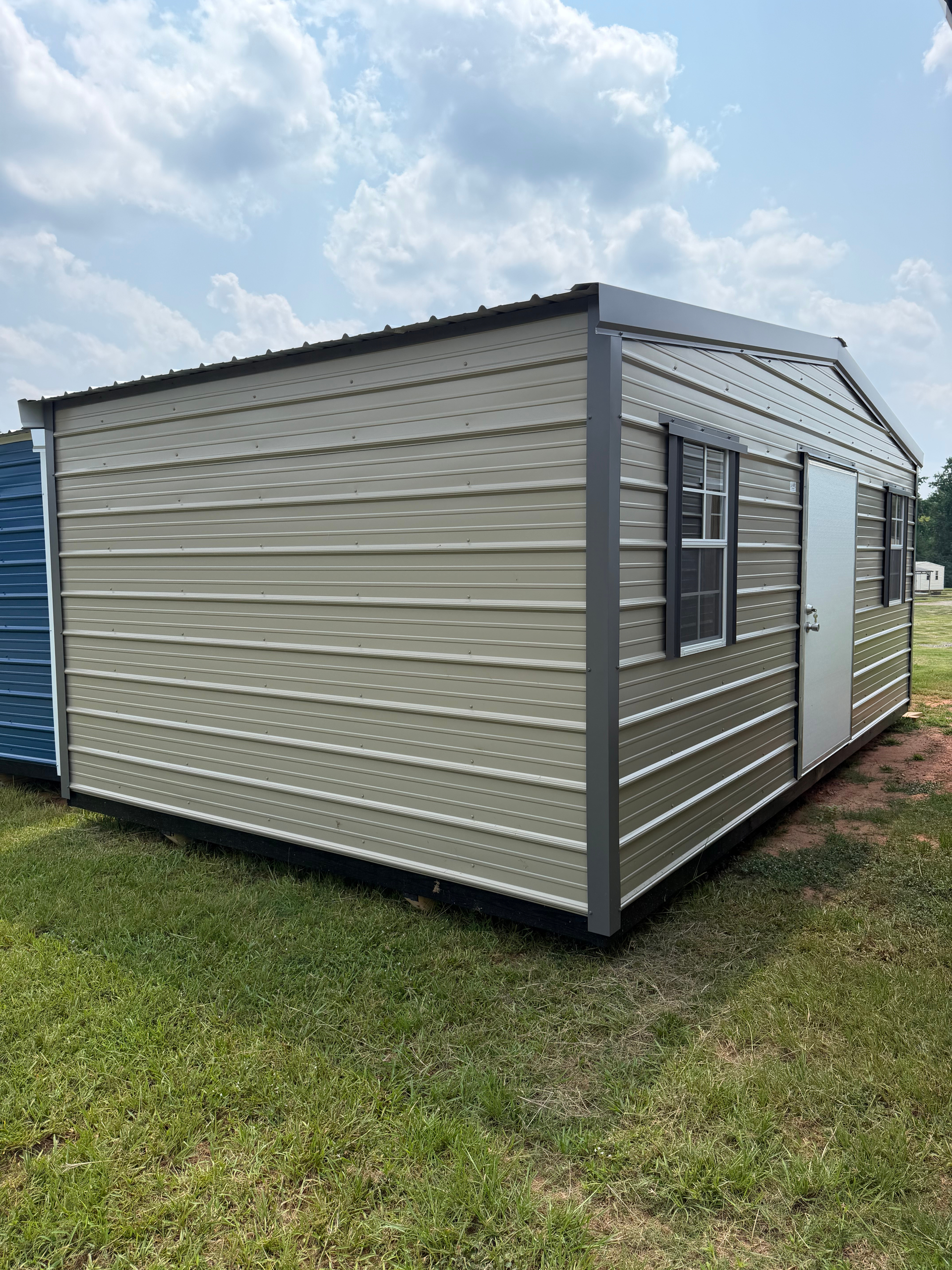 Beige portable storage shed with dark trim and a window, sitting on grass under a partly cloudy sky