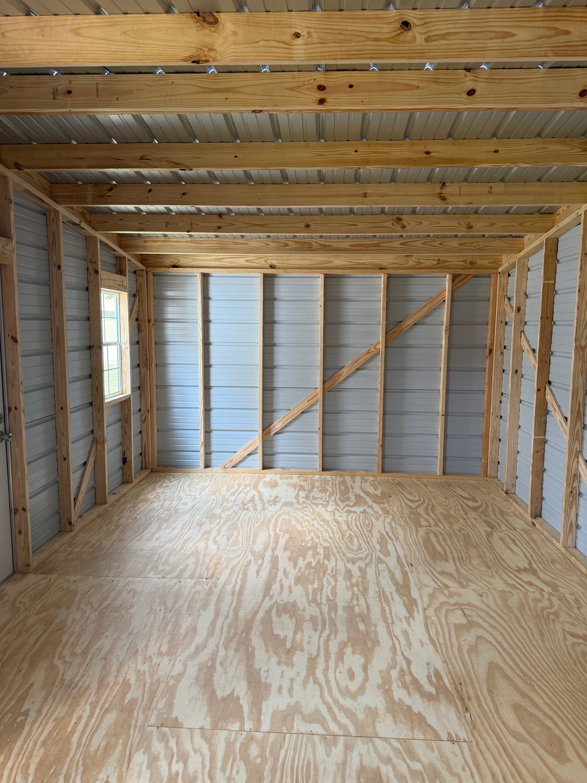 Empty wooden shed interior with plywood floor, exposed framing, and metal wall panels