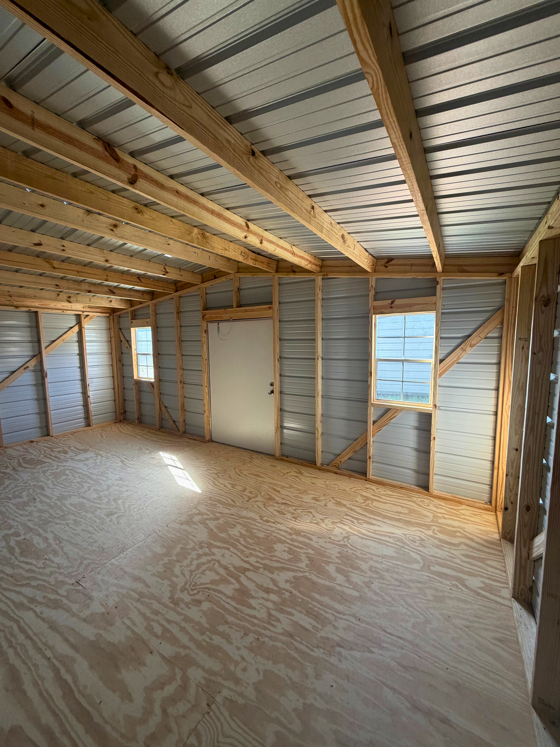 Empty unfinished room with exposed wooden studs, roof beams, and plywood subflooring.