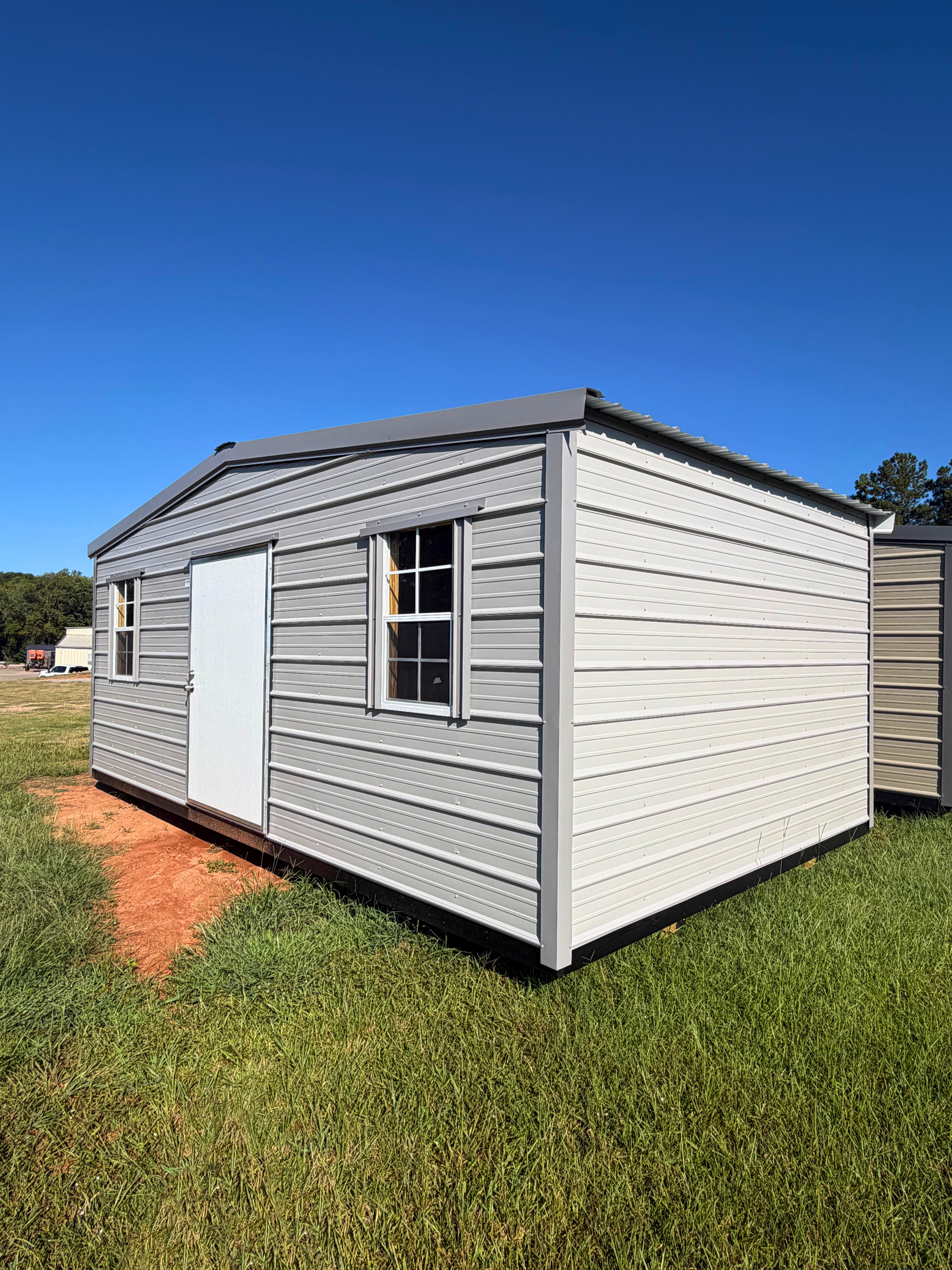 Small white shed with gray roof and trim, standing on grass under a clear blue sky.