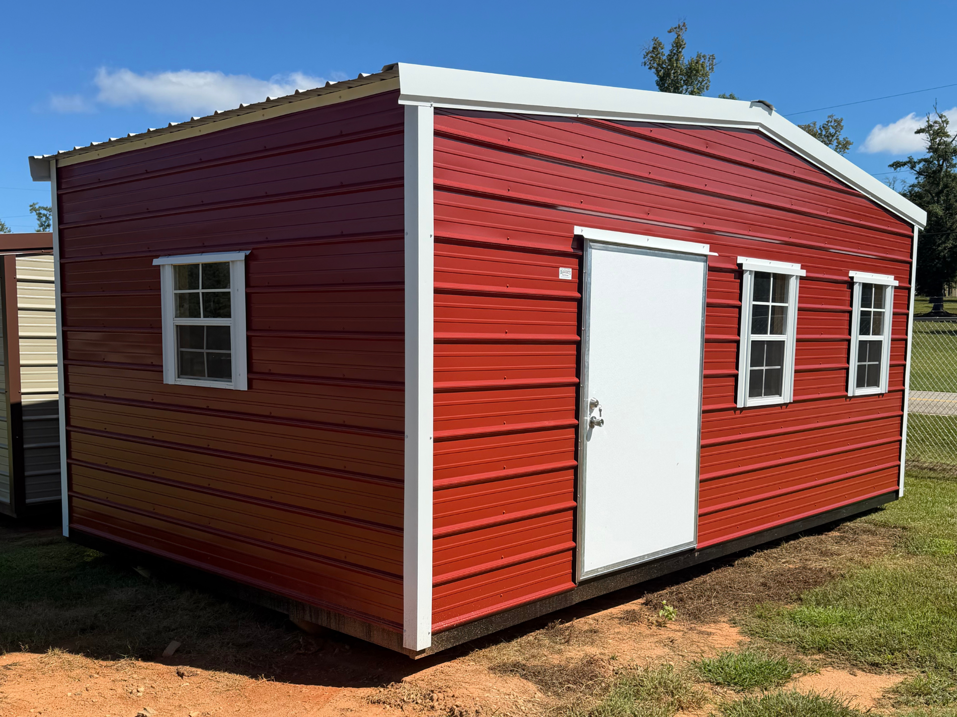 Red portable shed with white door and windows on a dirt lot under a blue sky