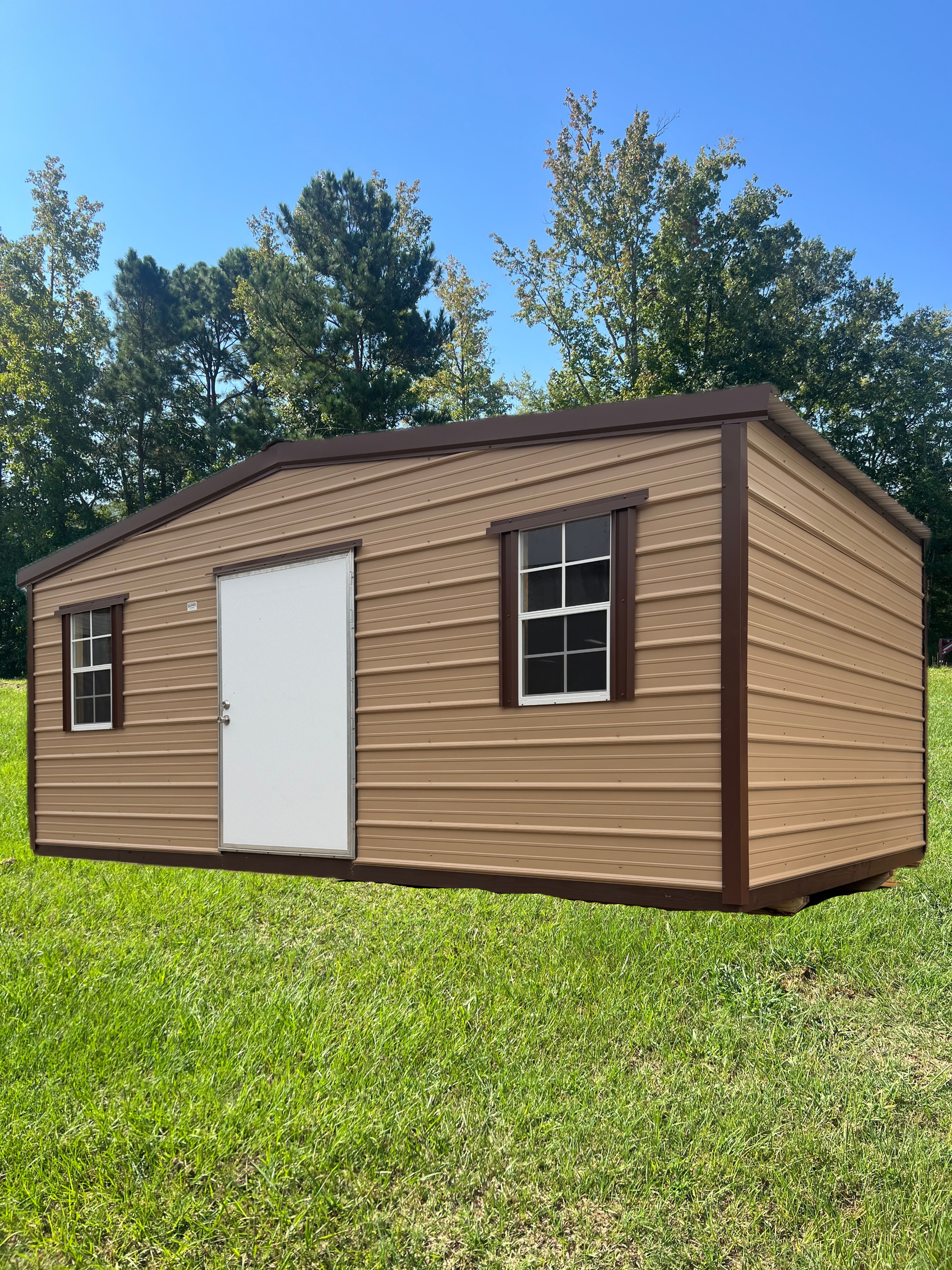 Small tan shed with white door and windows on a grassy lawn under a blue sky