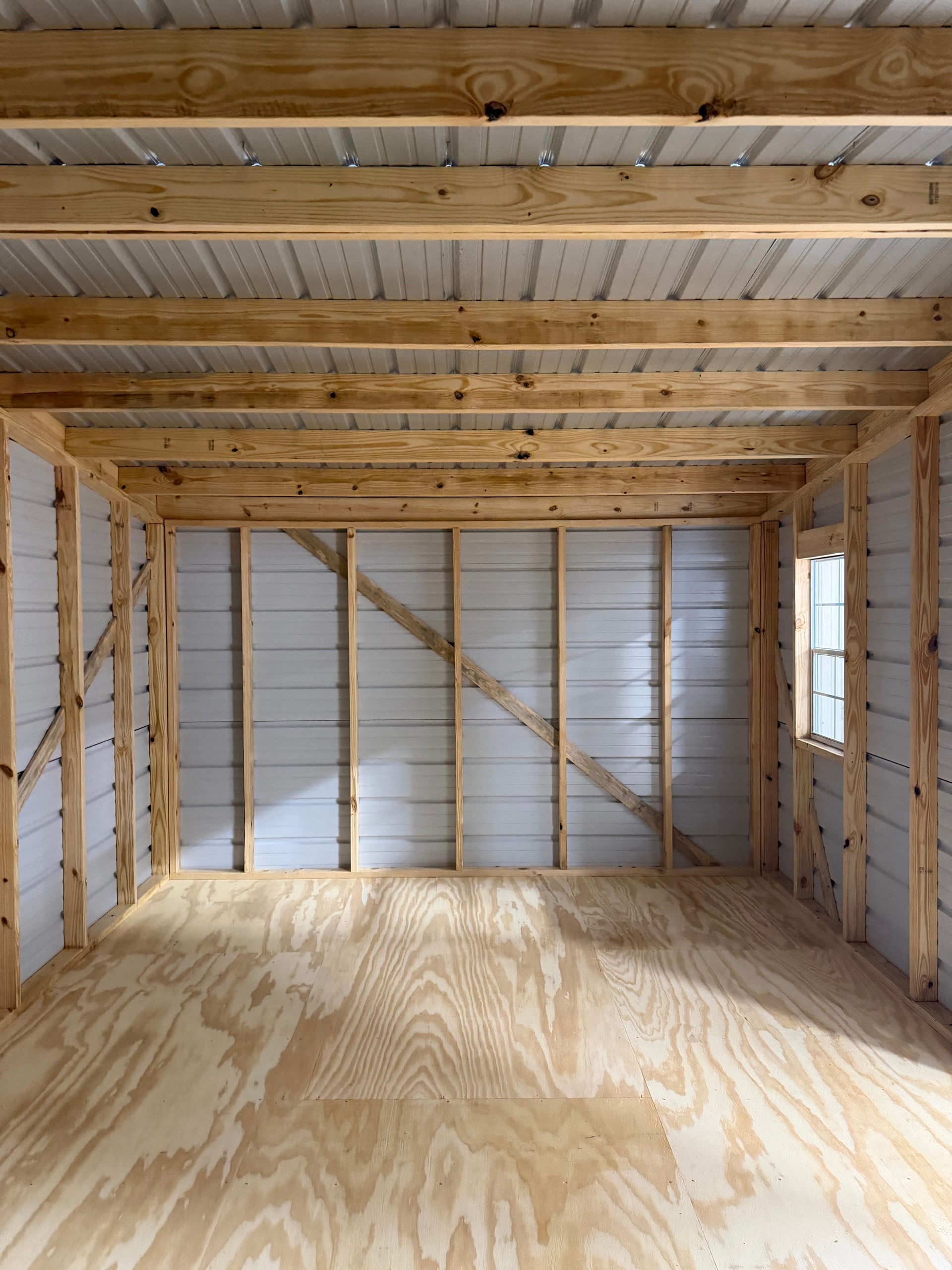 Empty unfinished wood-framed room with plywood floor and exposed beams