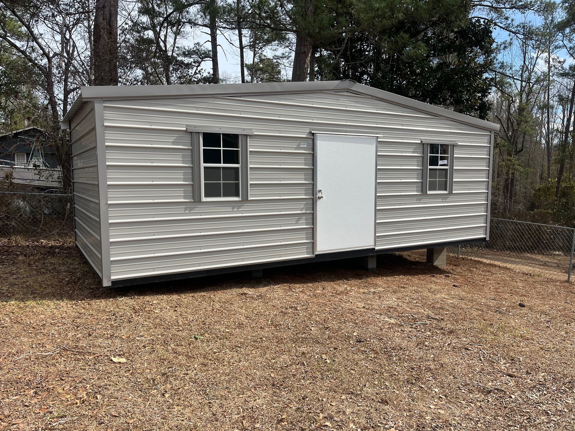 Gray metal shed with a white door and two windows on a brown lot.