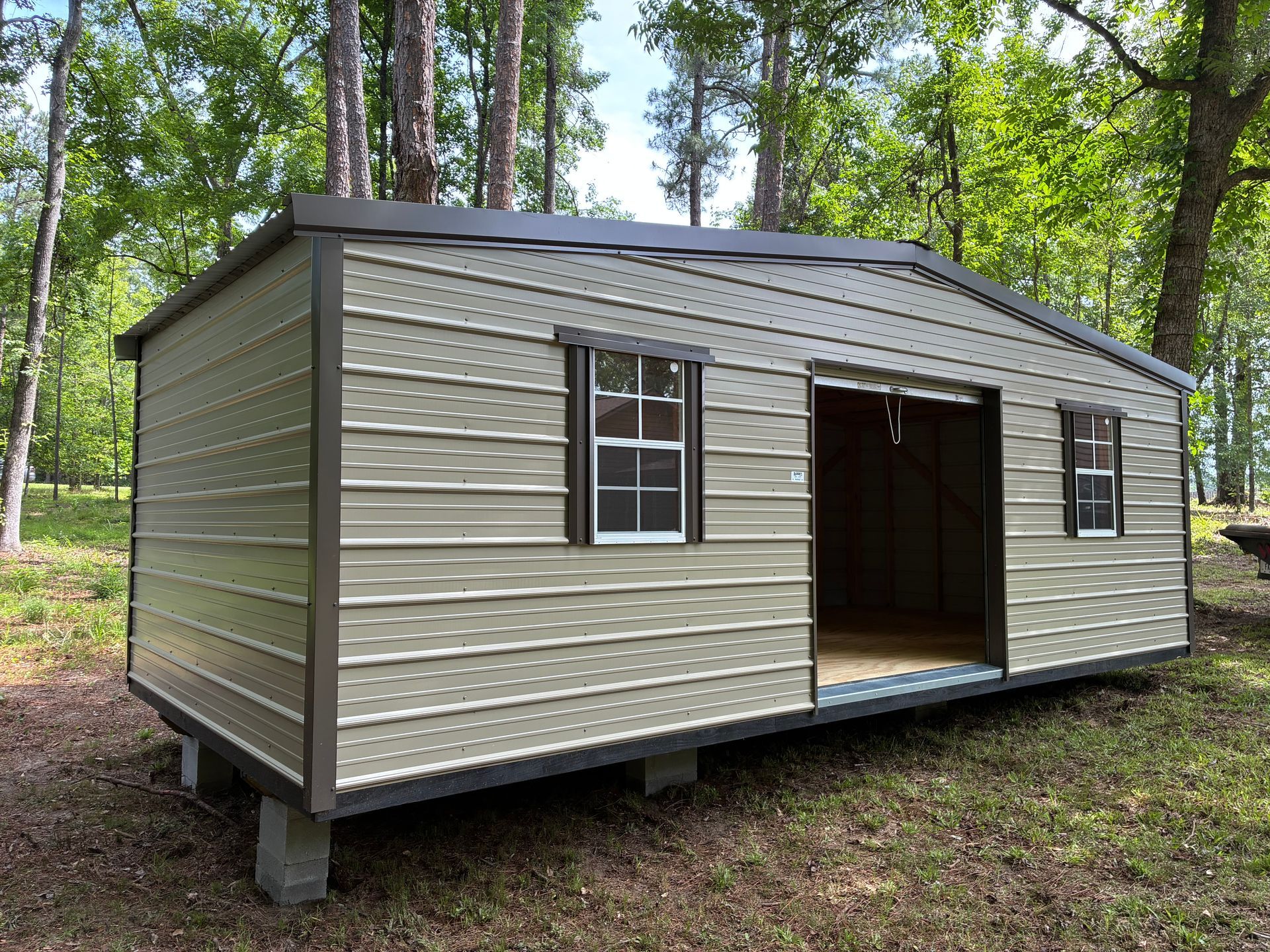 Small beige shed-style building with a metal roof and open doorway in a wooded area