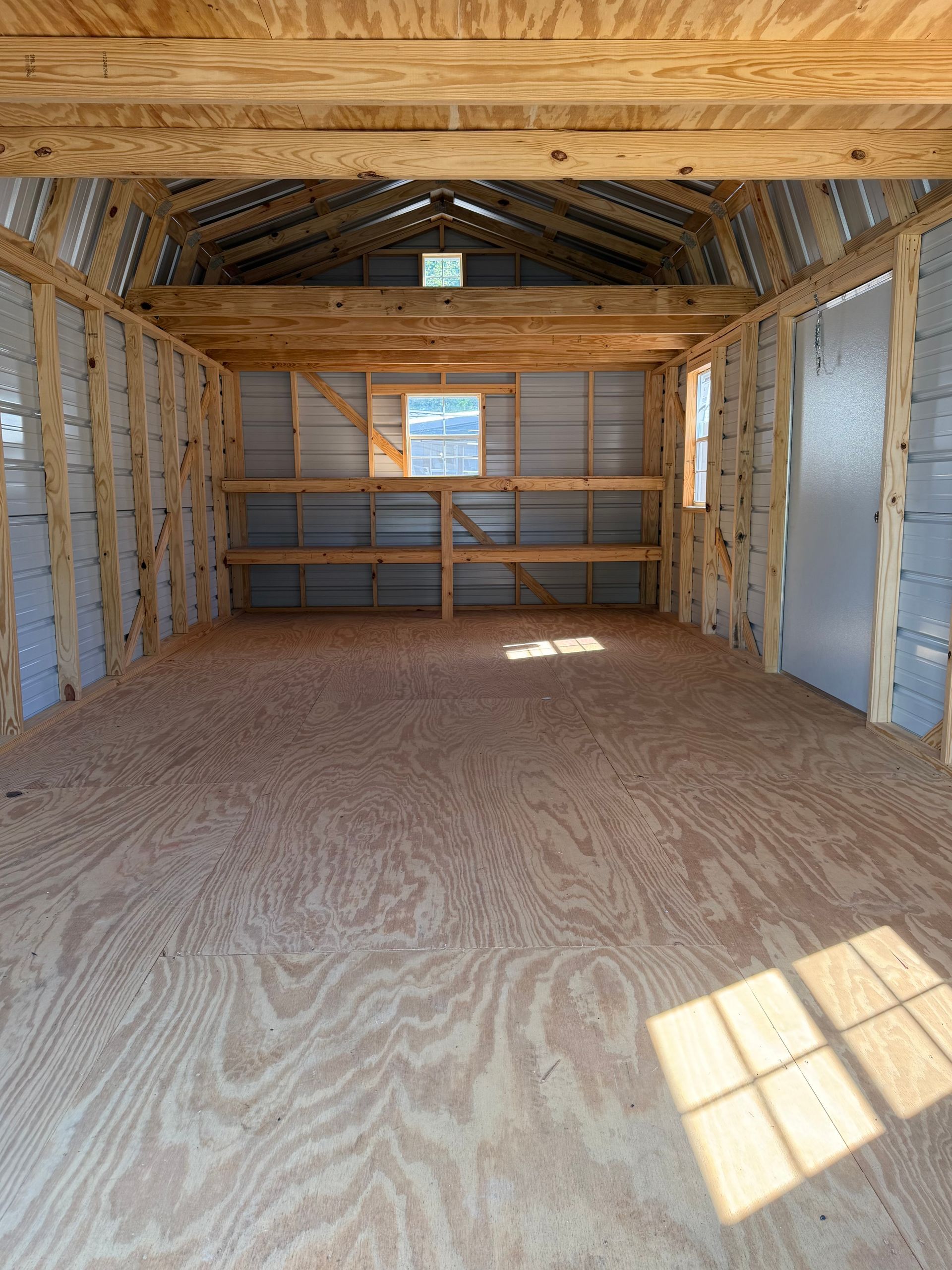 Empty unfinished room interior with exposed framing, plywood floor, and sunlight on the floor