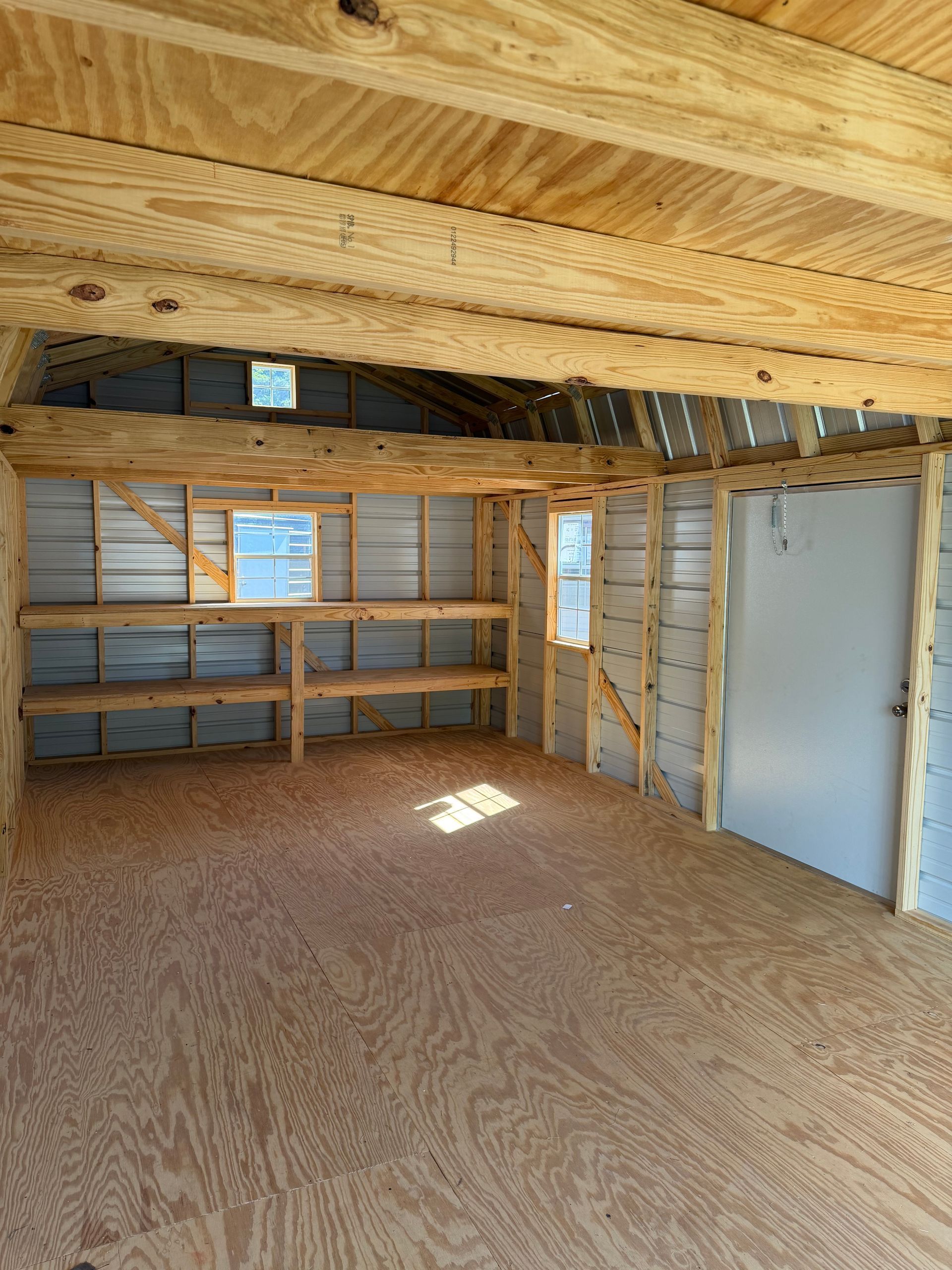 Empty unfinished shed interior with plywood floor, exposed wood framing, and corrugated metal walls.