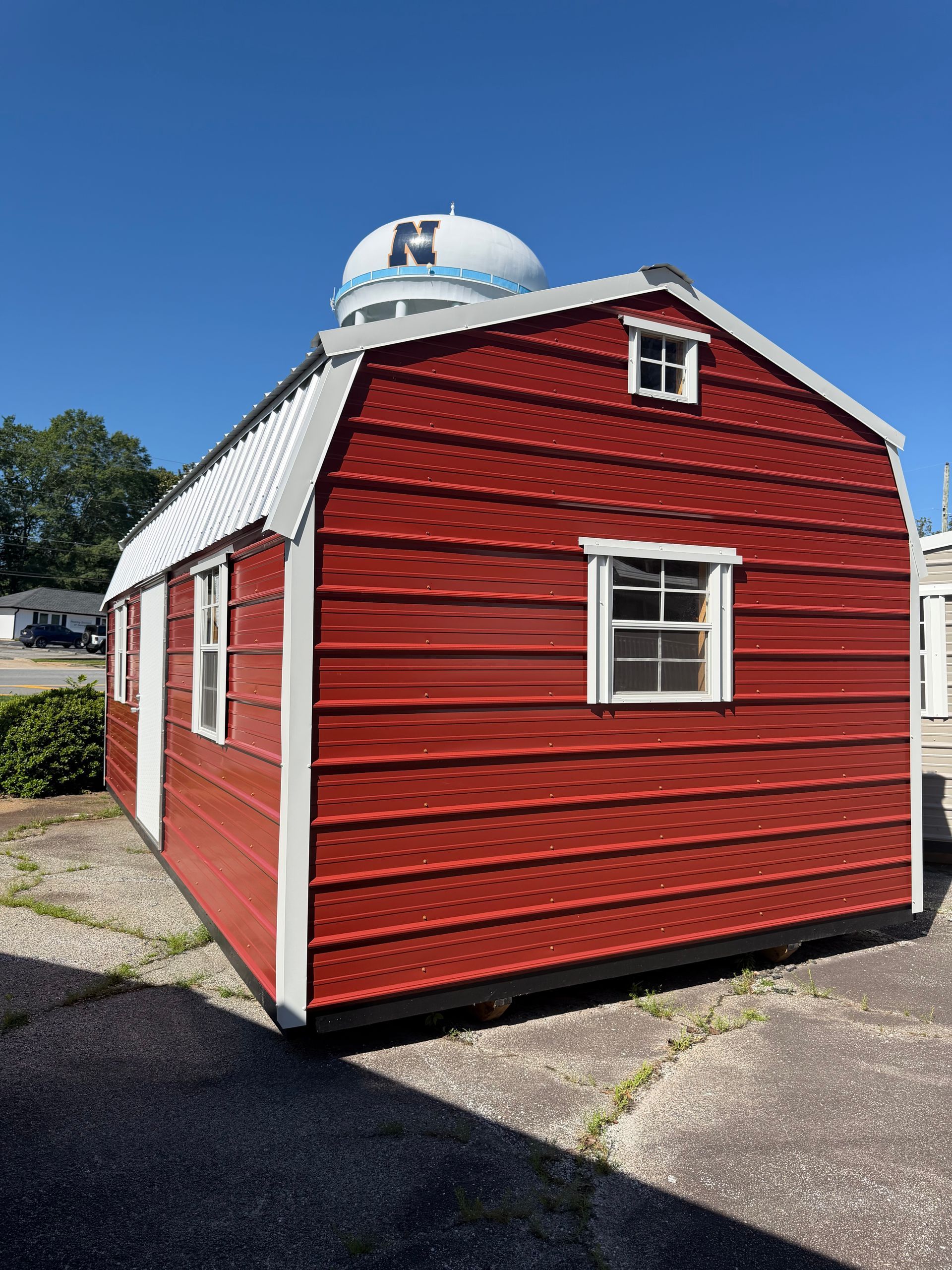 Red barn-style shed with white trim and a small cupola on a gravel lot under a blue sky