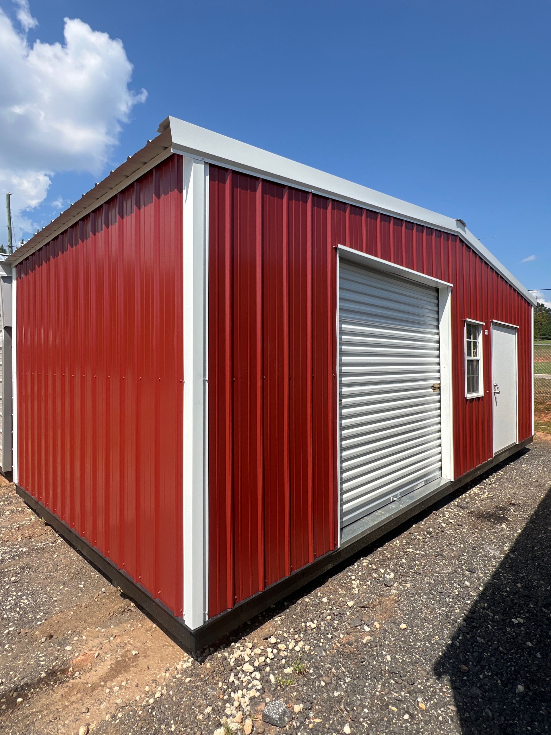Red metal storage building with white trim and a roll-up garage door under a blue sky.