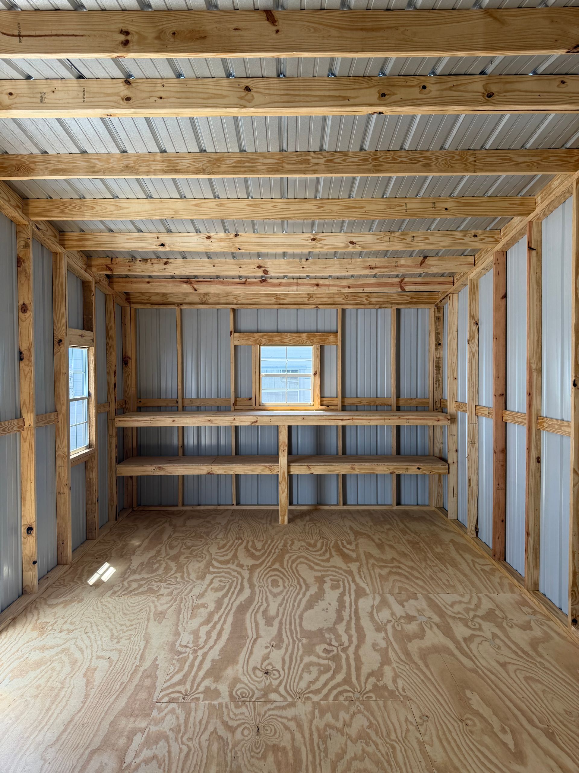Unfinished wooden room interior with plywood floor, exposed framing, and a small window at the back