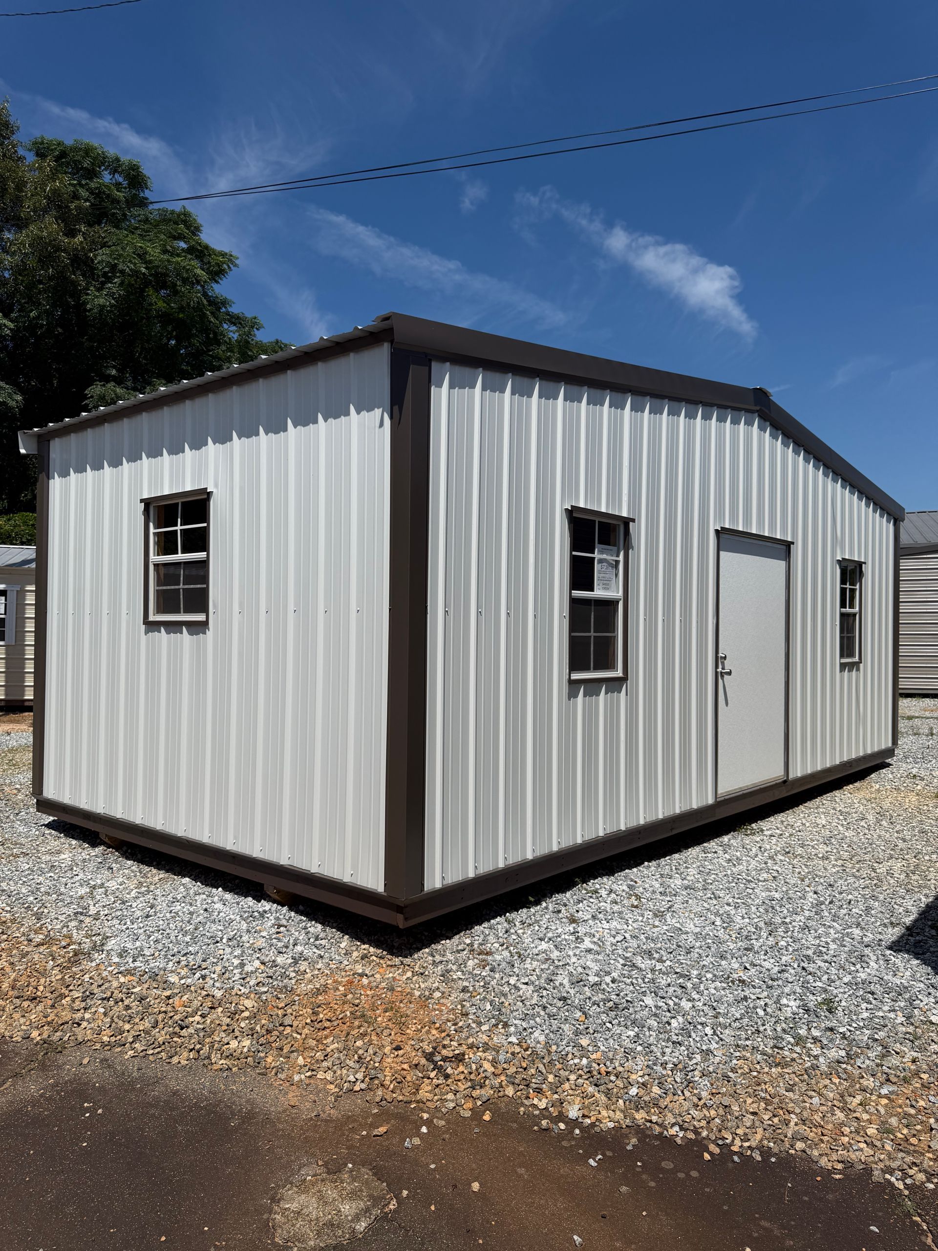 Small beige metal portable building on gravel under a blue sky