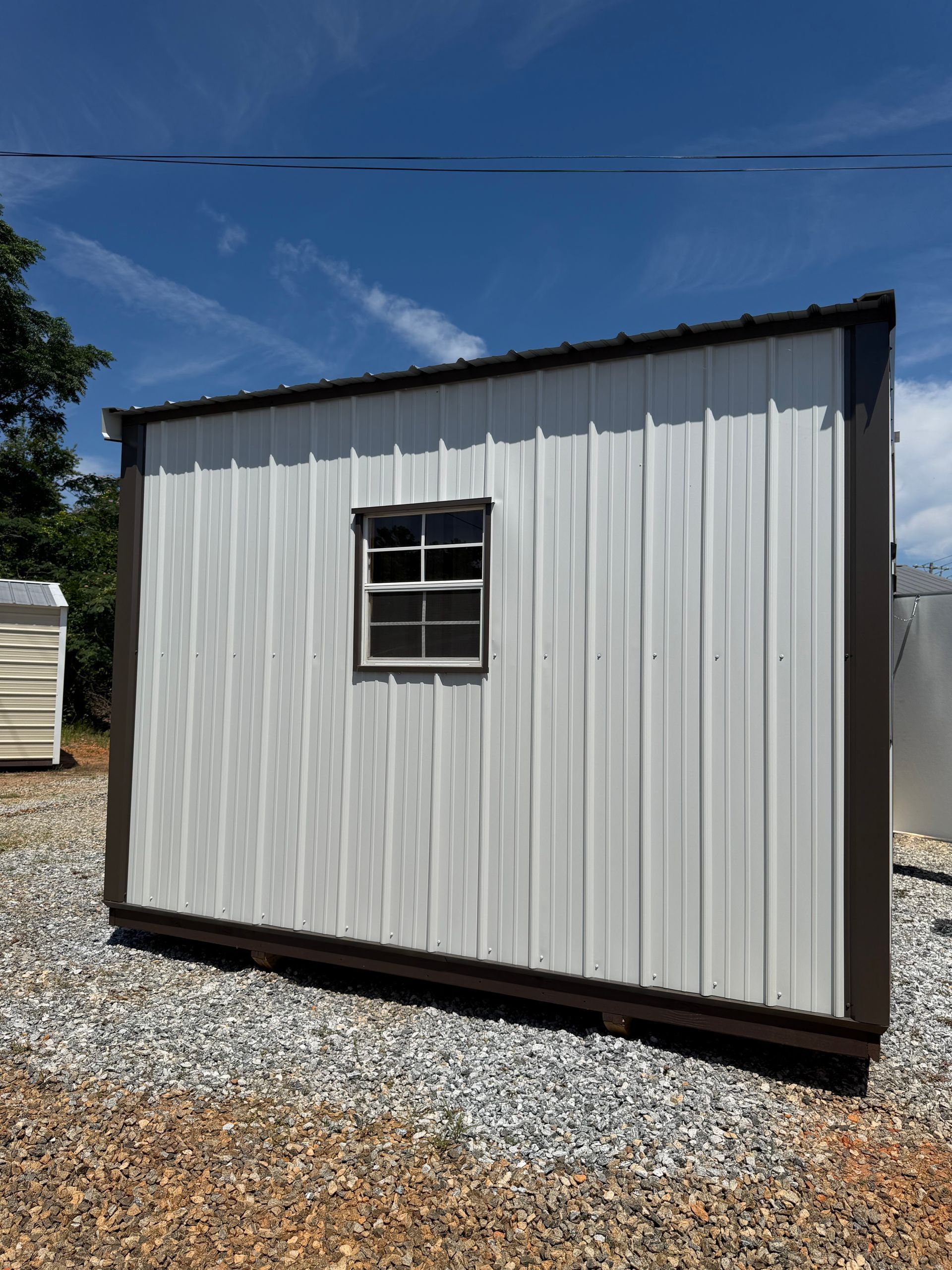 Small white shed with a window on a gravel lot under a blue sky