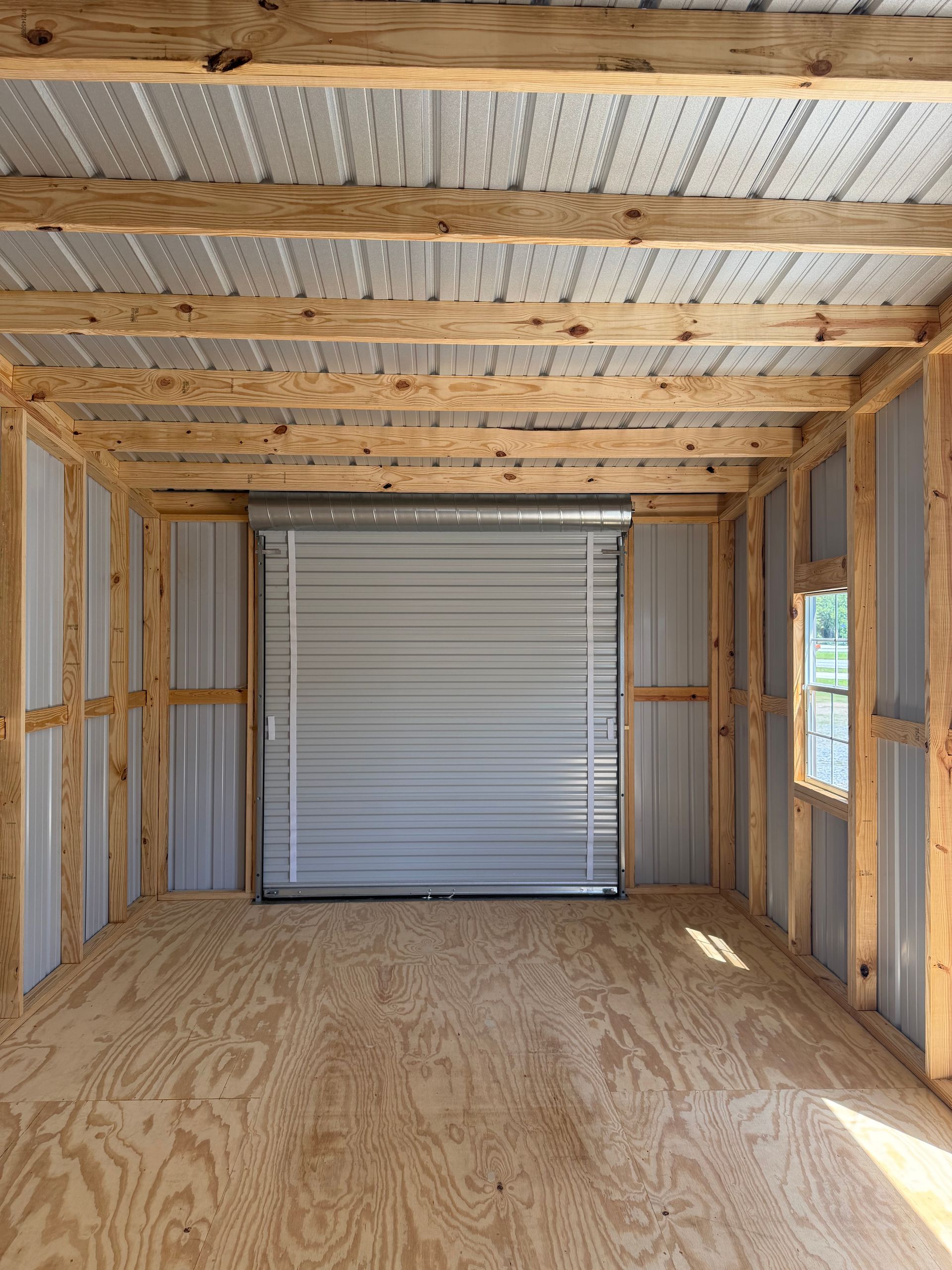 Interior of unfinished wooden shed with plywood floor and a closed roll-up garage door