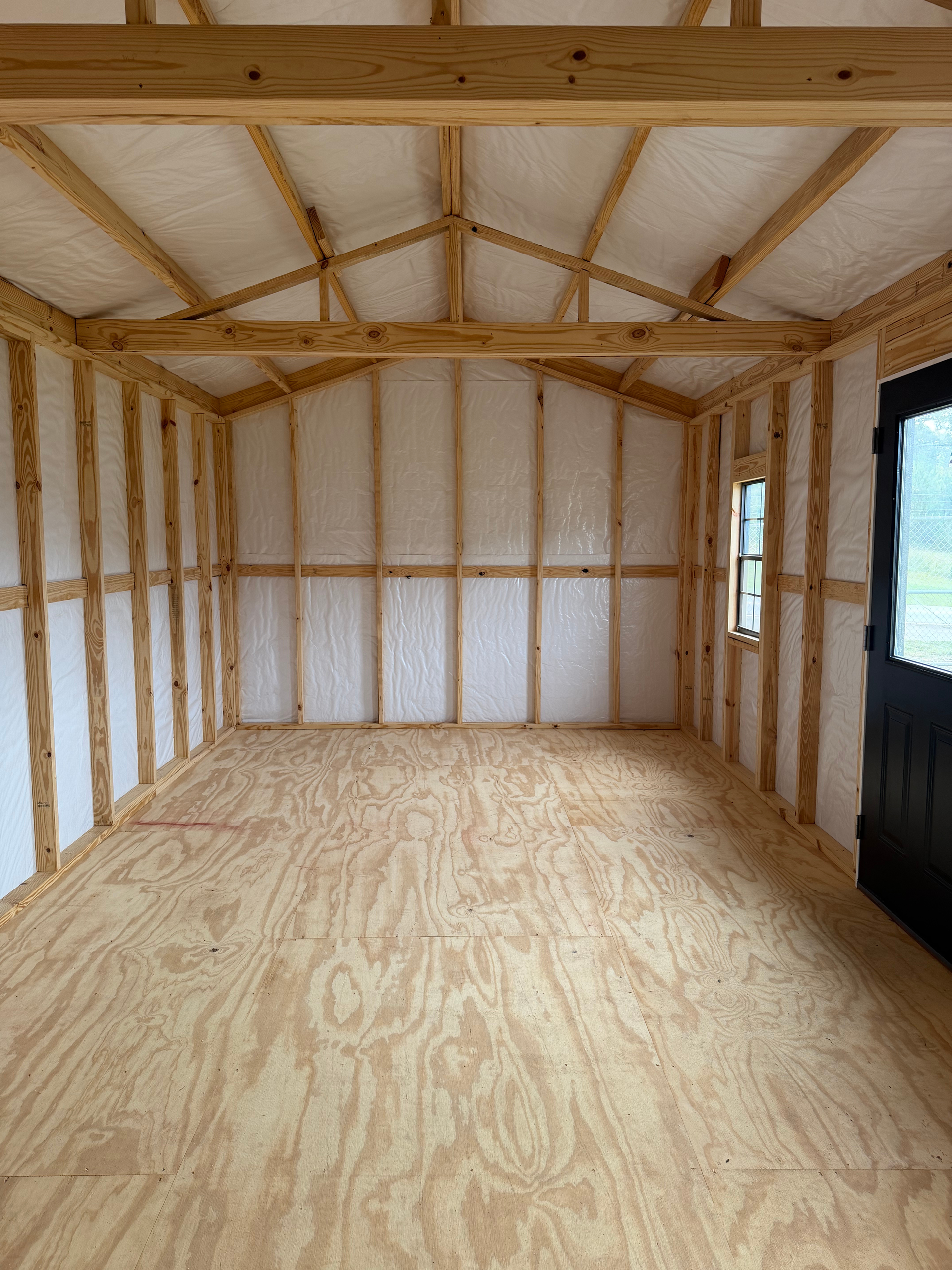 Empty unfinished room with plywood floor, exposed wood framing, and insulated walls and ceiling.