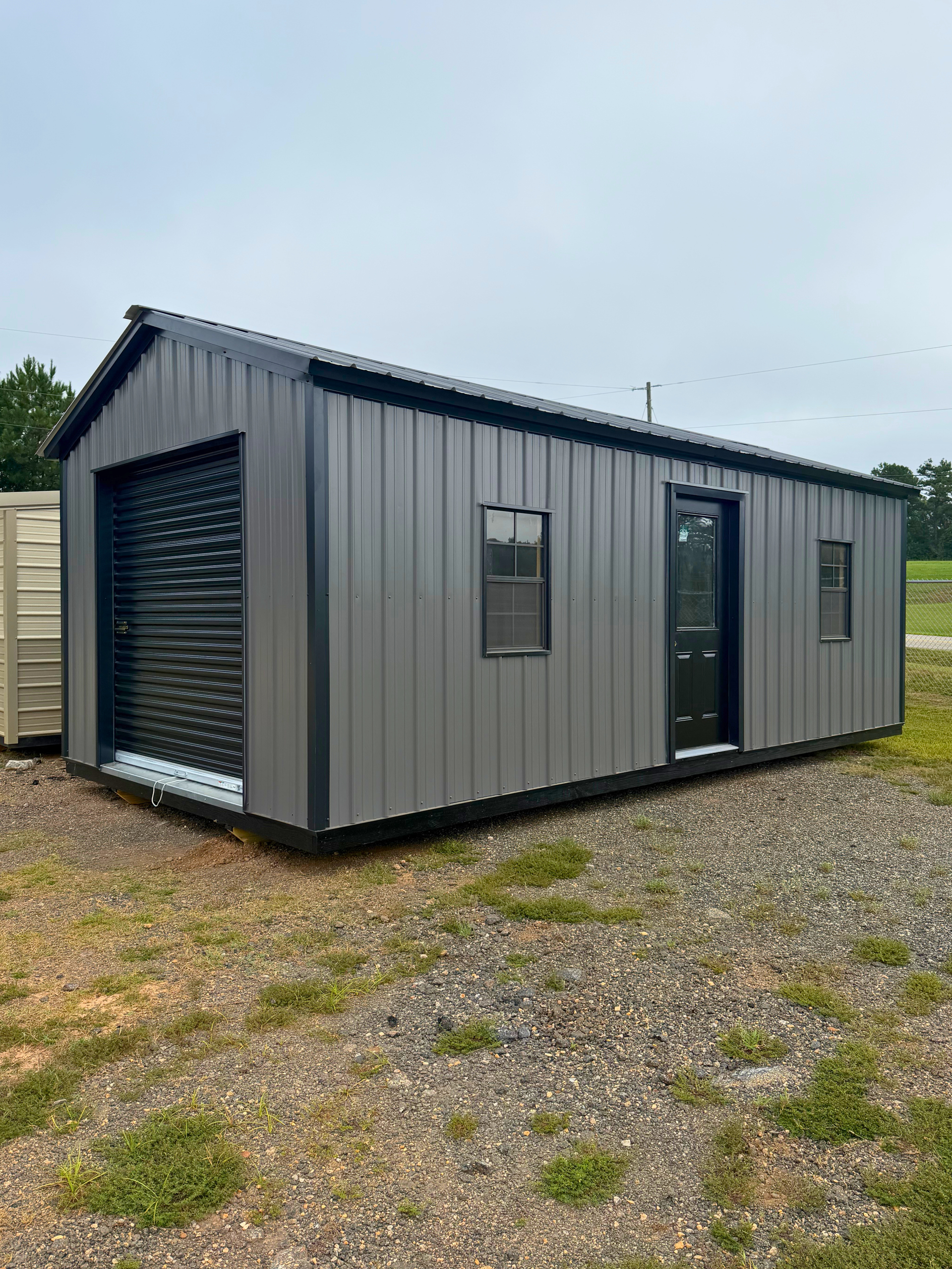 Gray metal tiny house with black doors and windows on a gravel lot under a cloudy sky