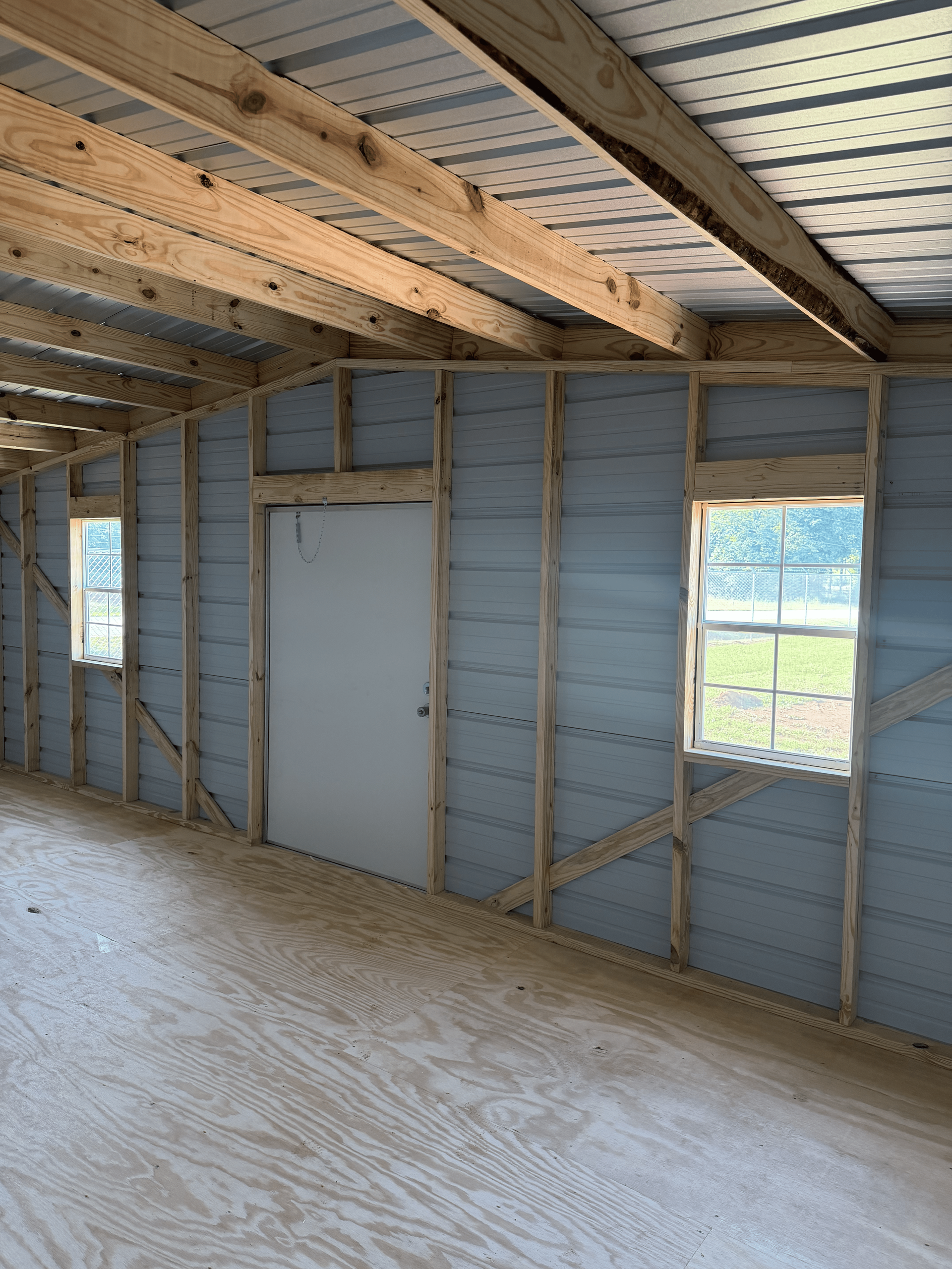 Interior of unfinished room with exposed studs, blue wall insulation, a white door, and a window.